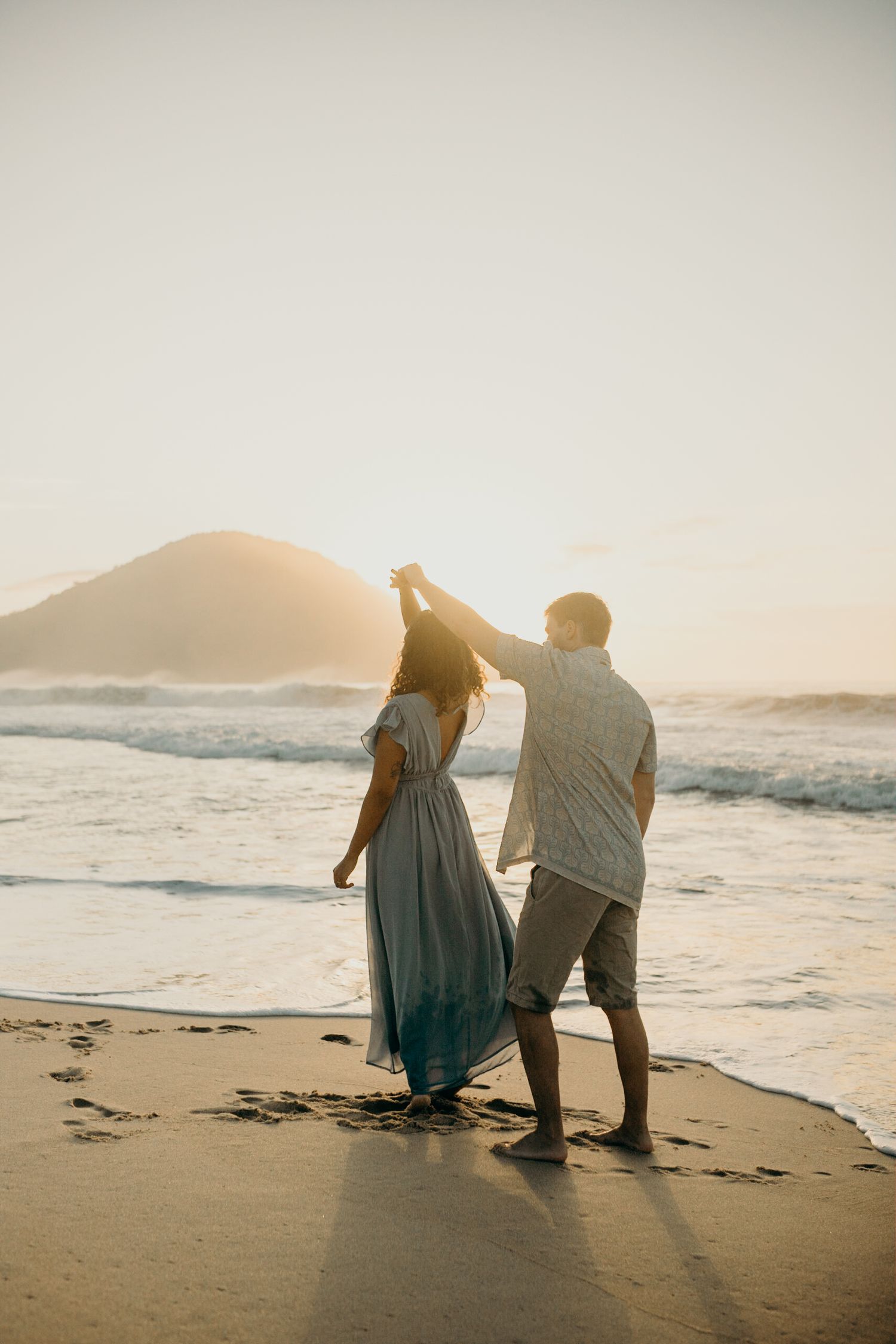 Couple dancing on beach during golden hour with mountain view.