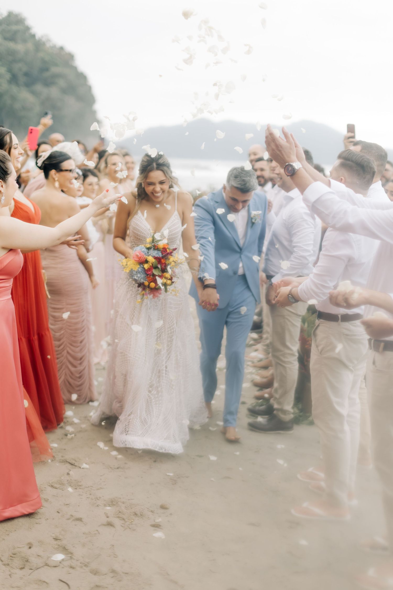 Joyful beach wedding celebration with guests throwing flower petals in the air.