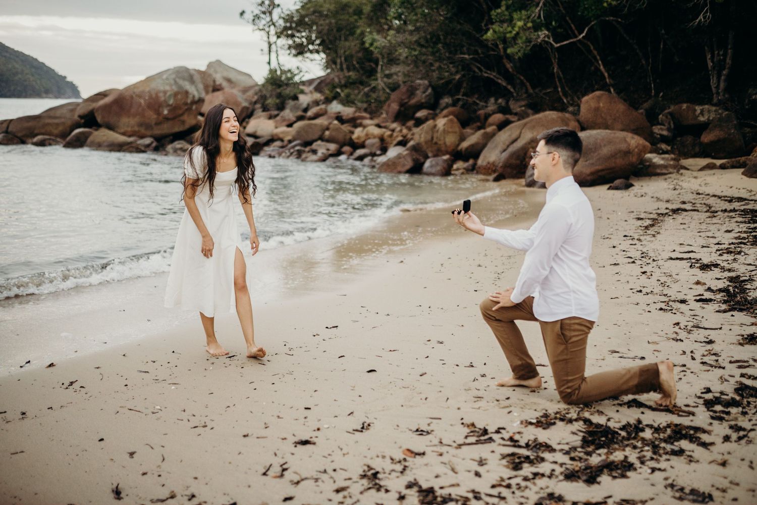 Proposal scene unfolds on scenic beach with rocky backdrop.