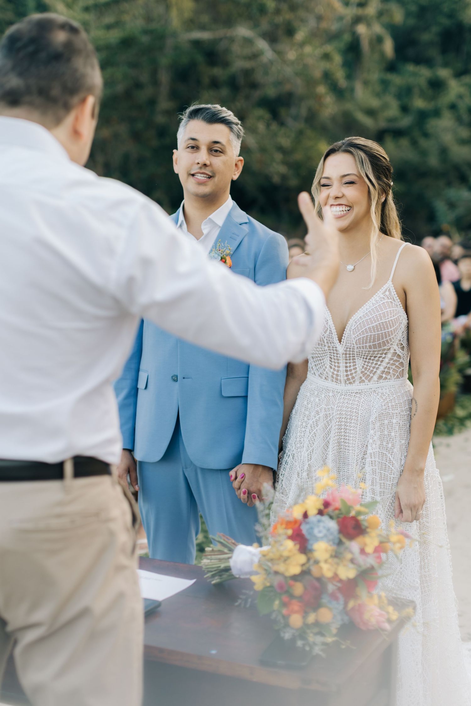 Wedding ceremony moment on beach with light blue suit and lace dress details.