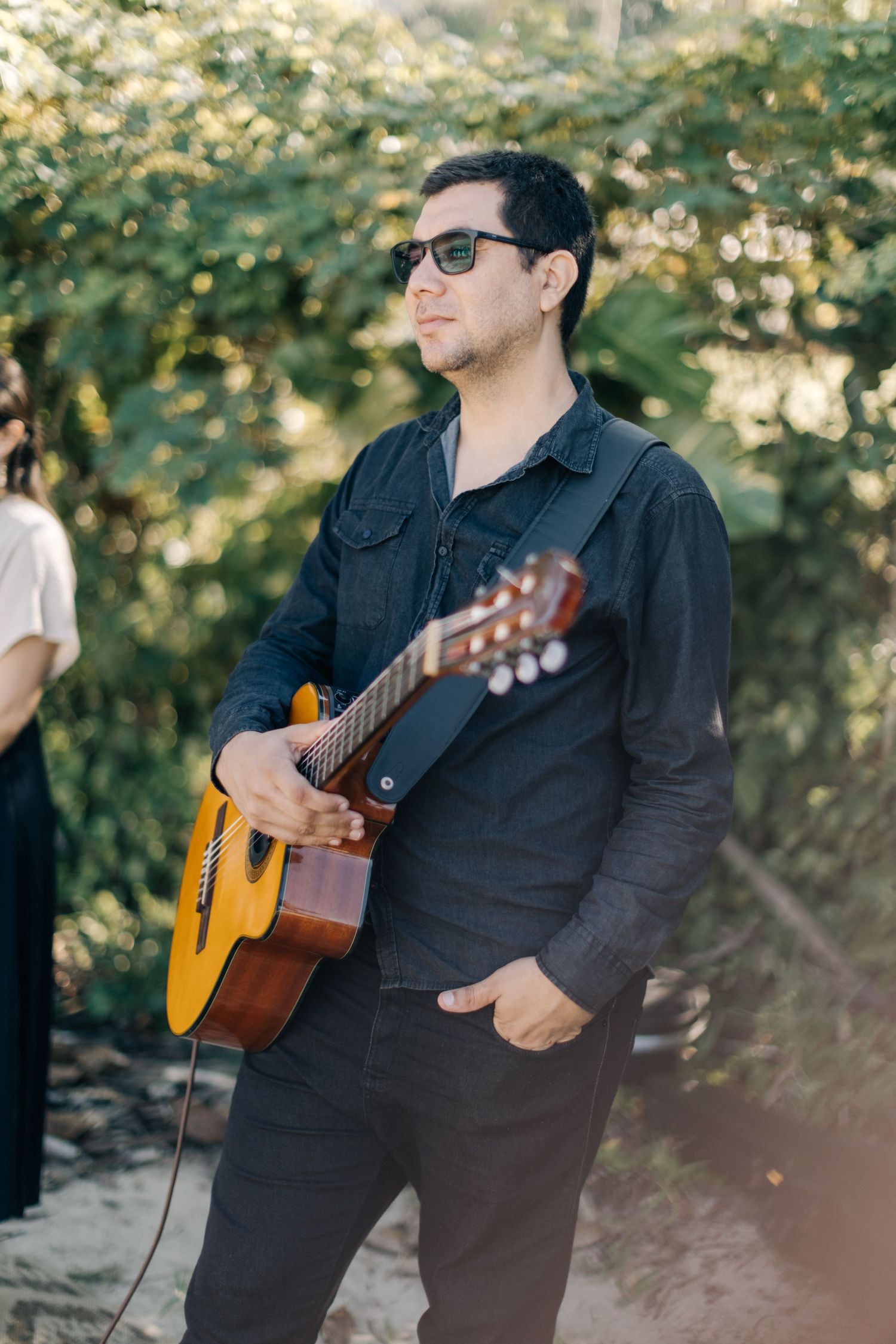 A musician plays acoustic guitar during an outdoor beach wedding ceremony.