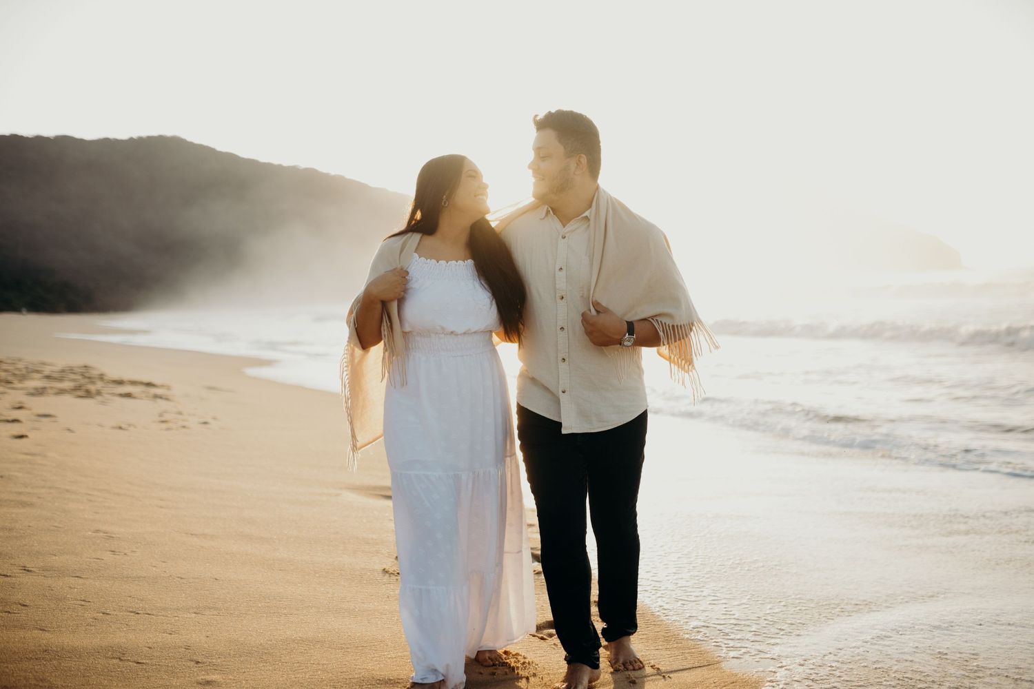 Two people share a romantic moment walking along the beach at golden hour.