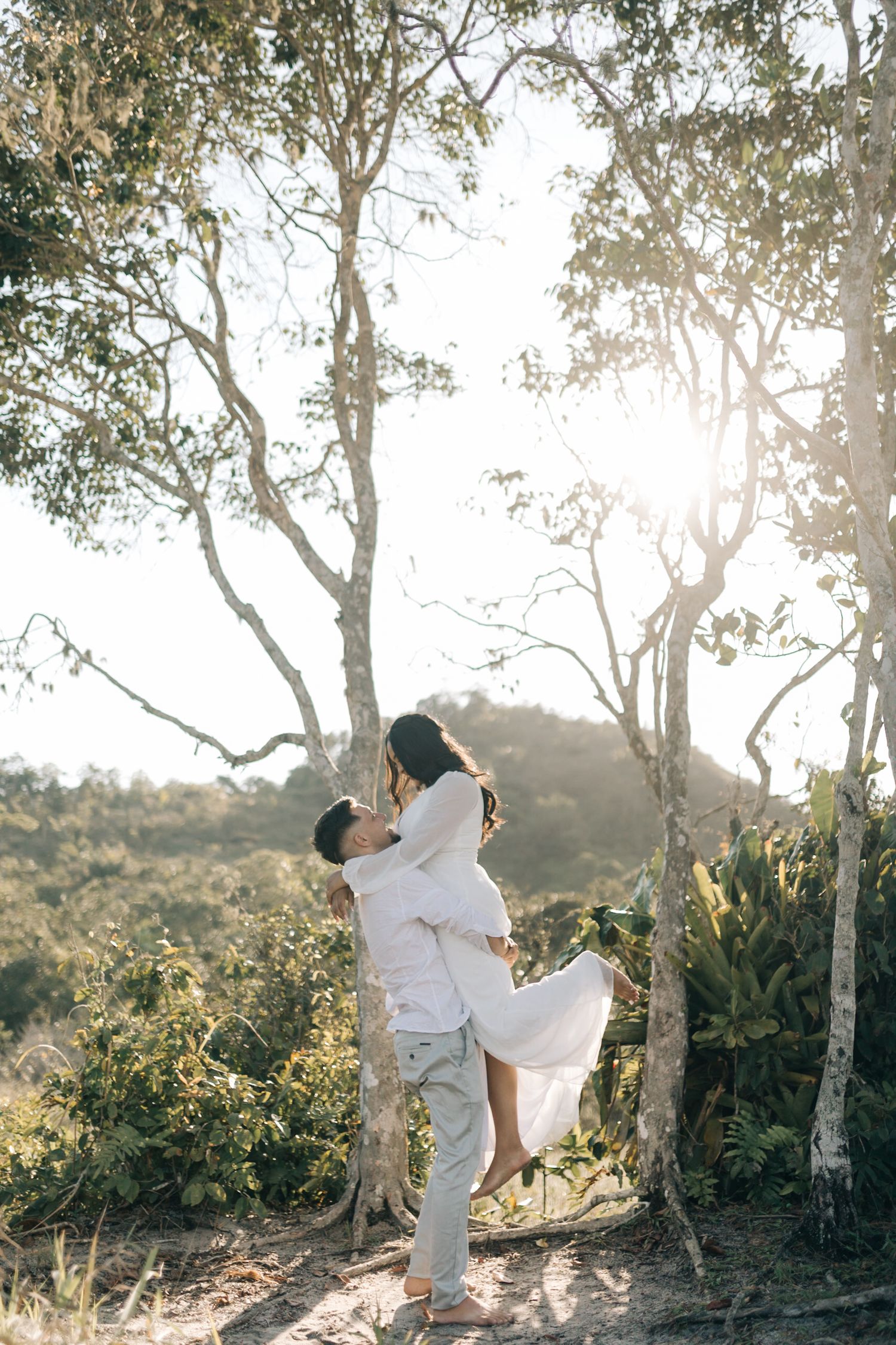 Sun-drenched portrait of a couple embracing among trees during a nature photoshoot.