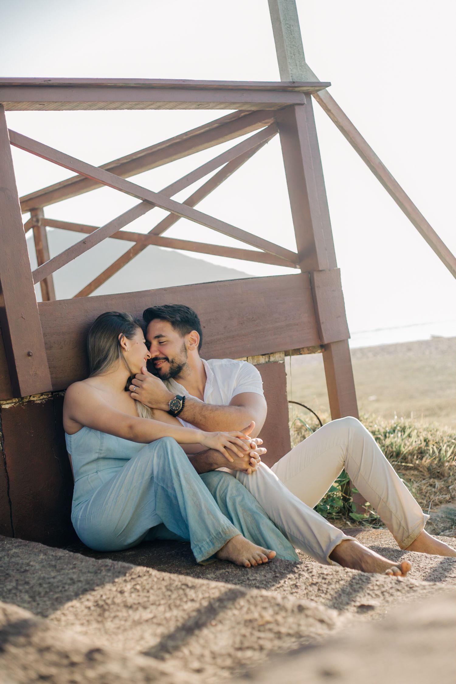 Affectionate couple in casual attire sharing tender moment on wooden deck at sunset.