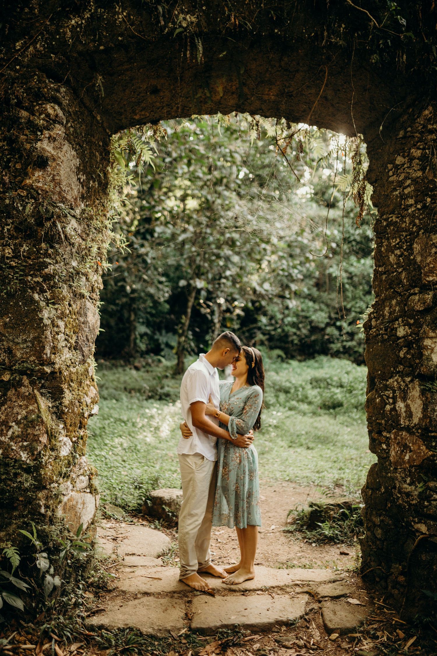 Romantic couple standing in a stone doorway surrounded by green foliage.