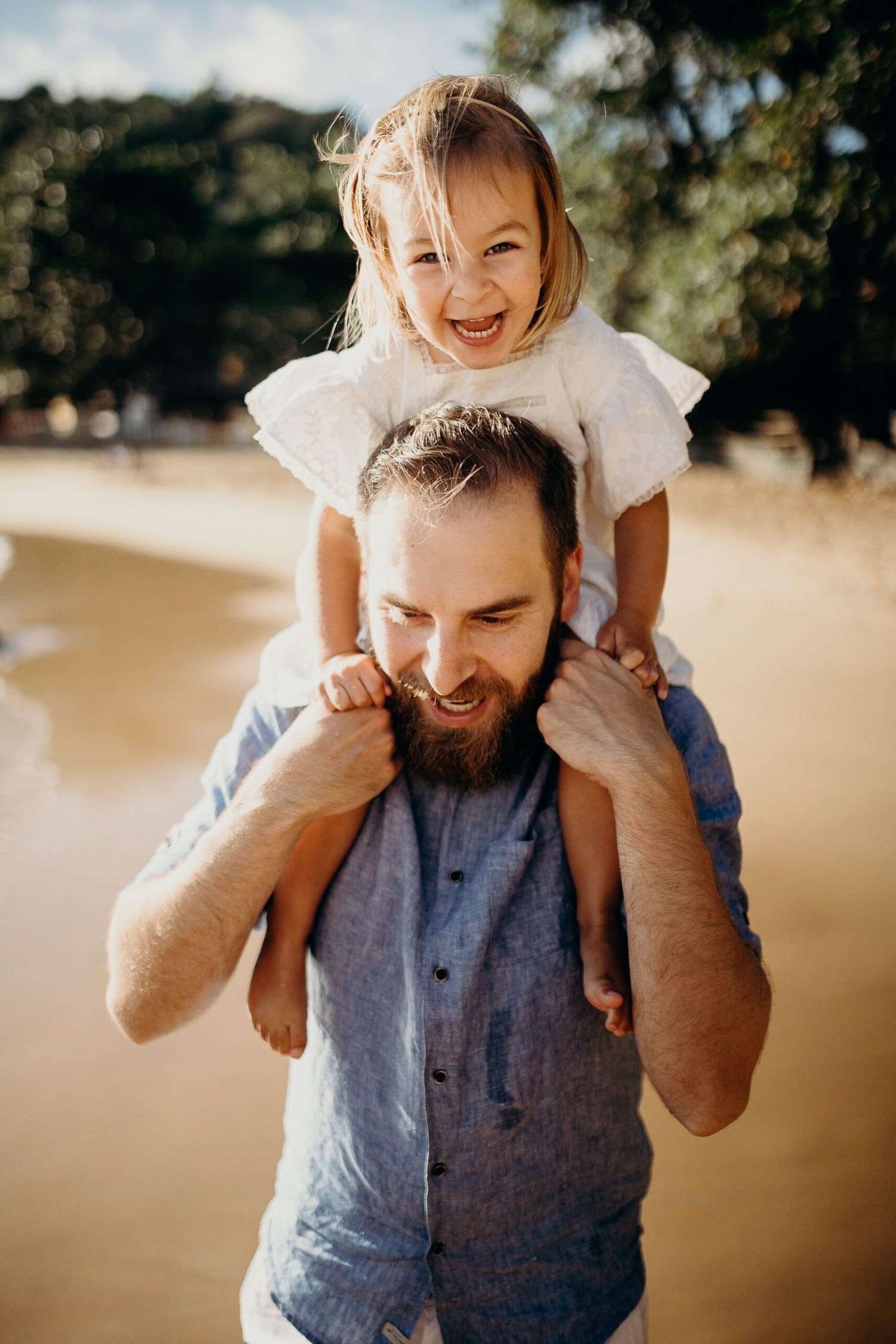 Parent giving shoulder ride to child on sandy beach during sunset.