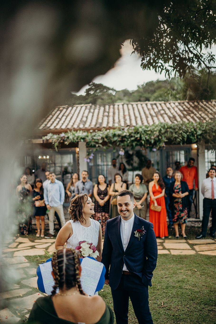 Wedding ceremony takes place on a beautiful lawn with guests watching from stone pathways.