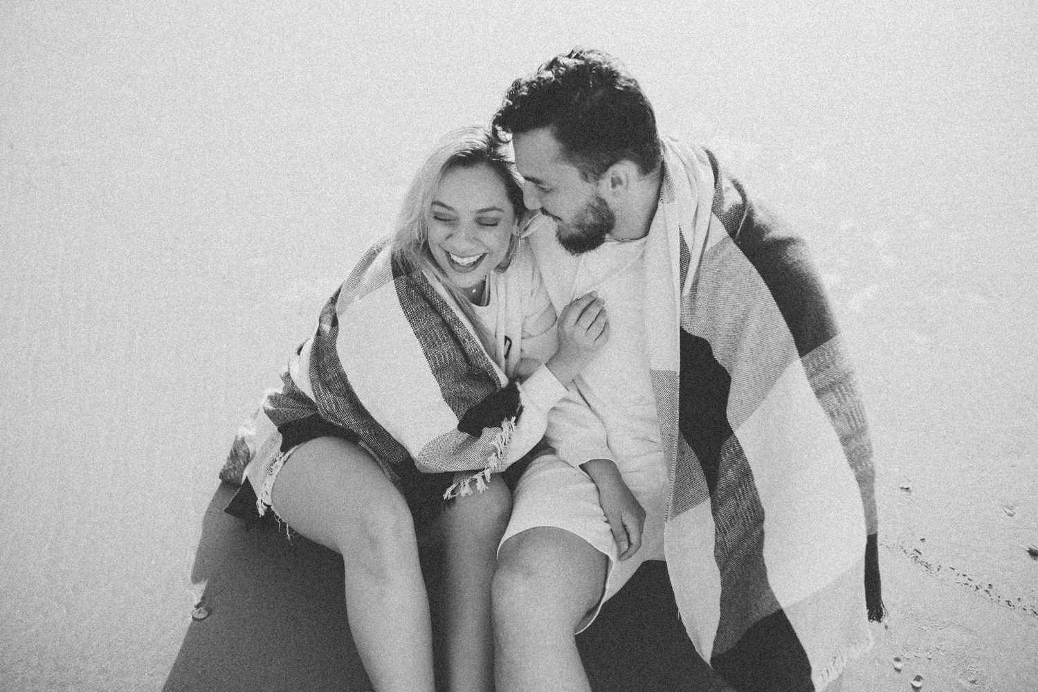 Black and white portrait of couple laughing together during beach photoshoot.
