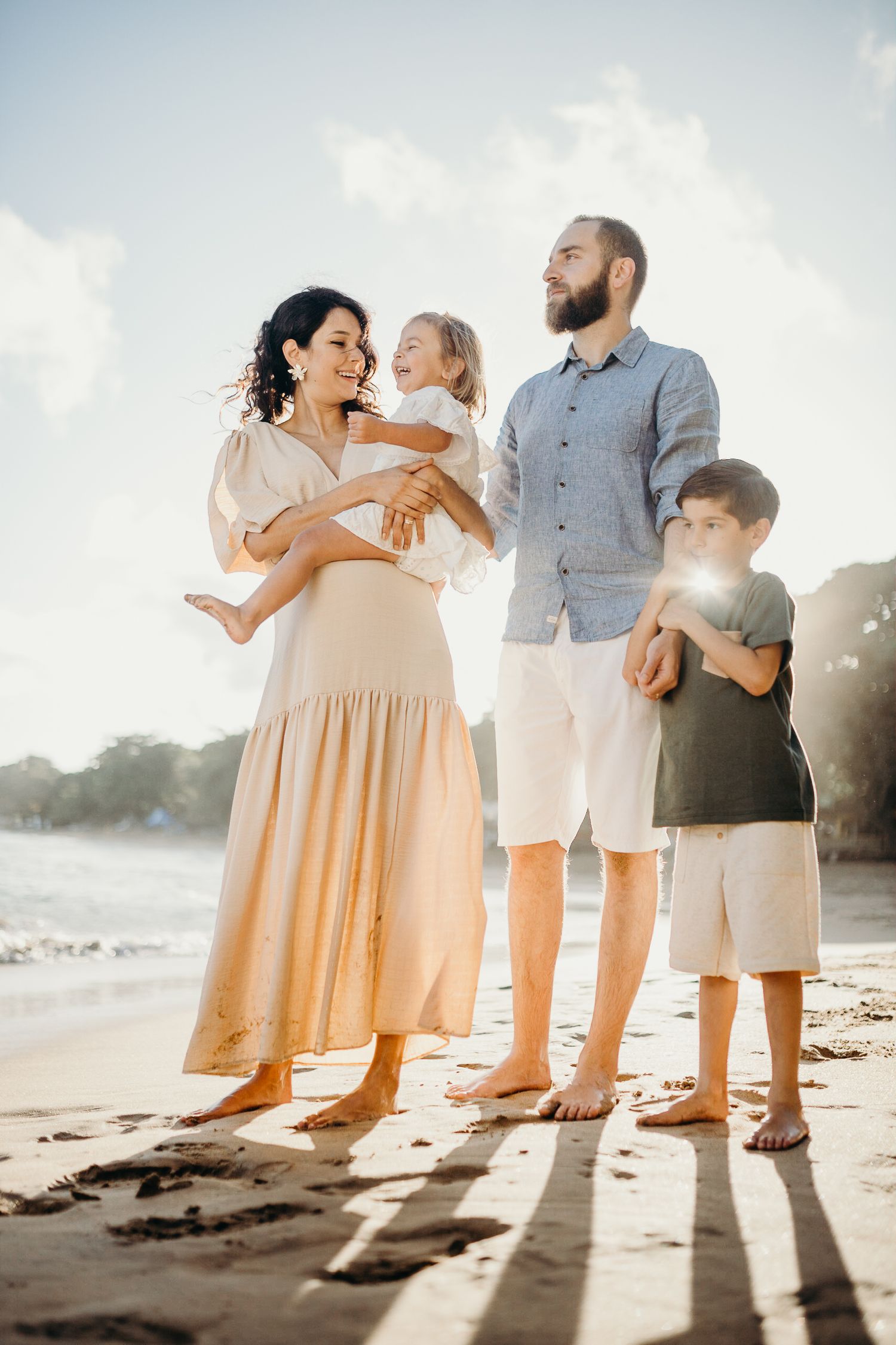 A family stands together on a beach at sunset with long shadows cast behind them.