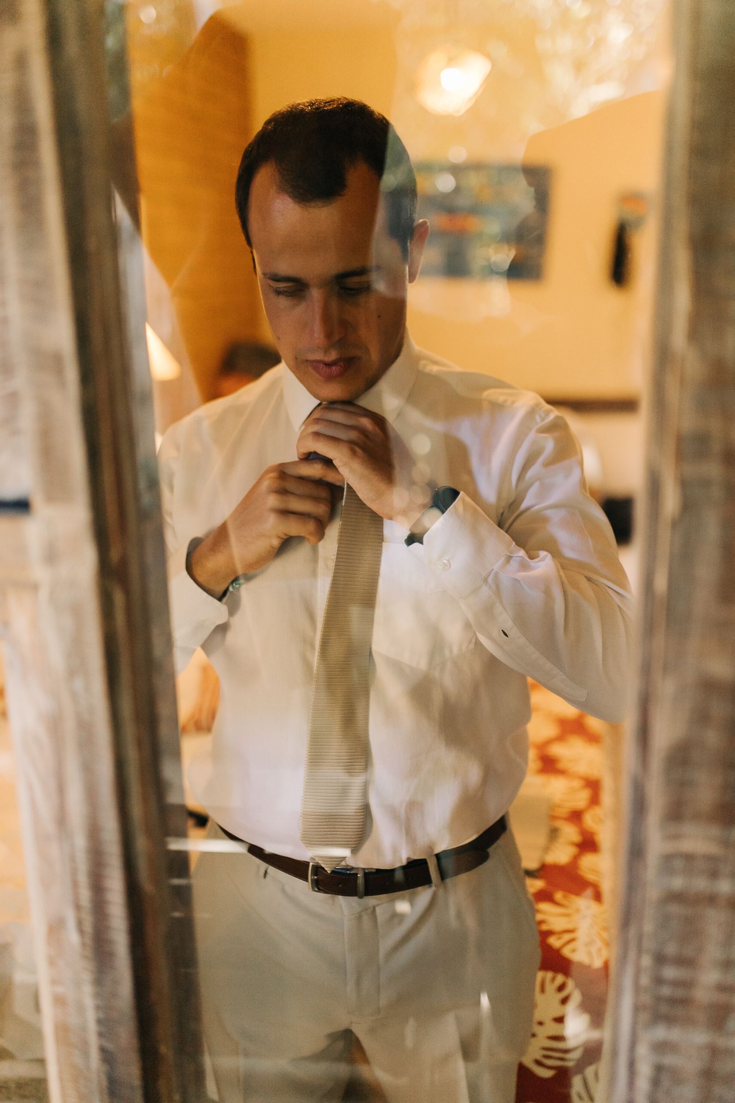 A person adjusts their tie while looking in a mirror wearing formal attire.