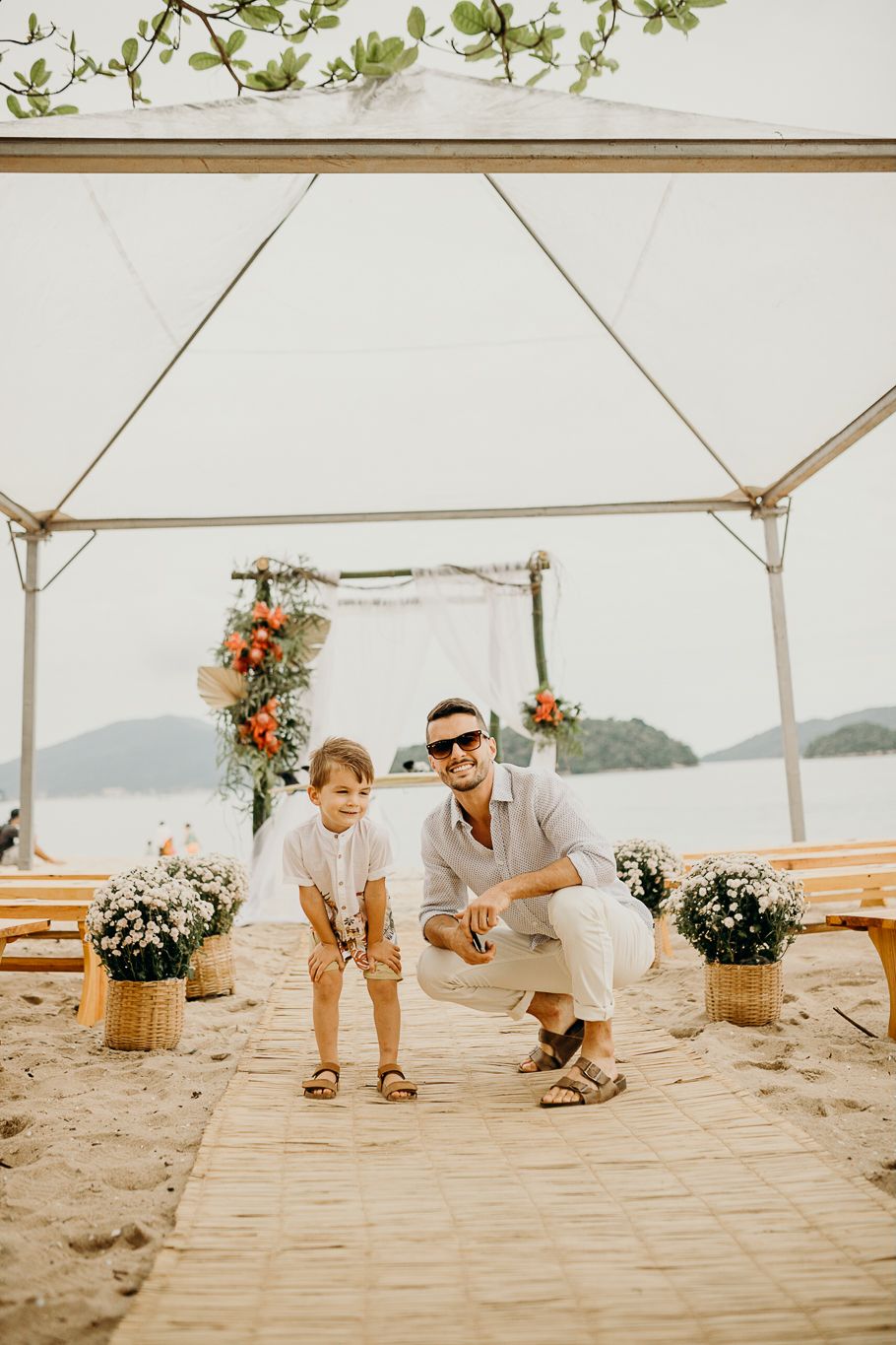 Minimalist beach wedding ceremony space with bamboo mat aisle and wooden benches.