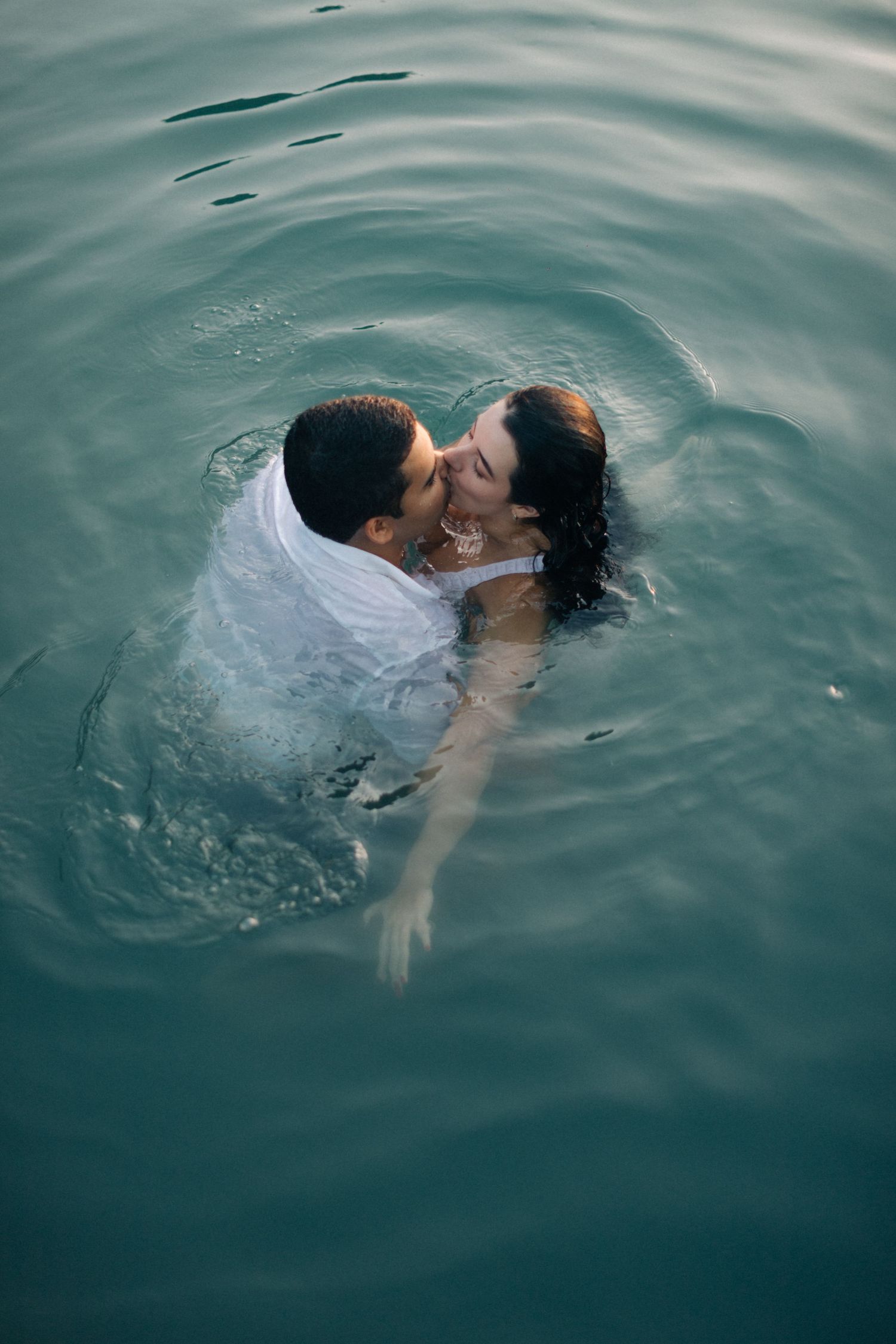 A couple shares an intimate moment while swimming in turquoise waters.