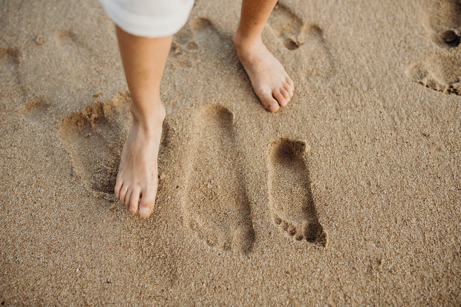 Close-up of feet and footprints in sandy beach.