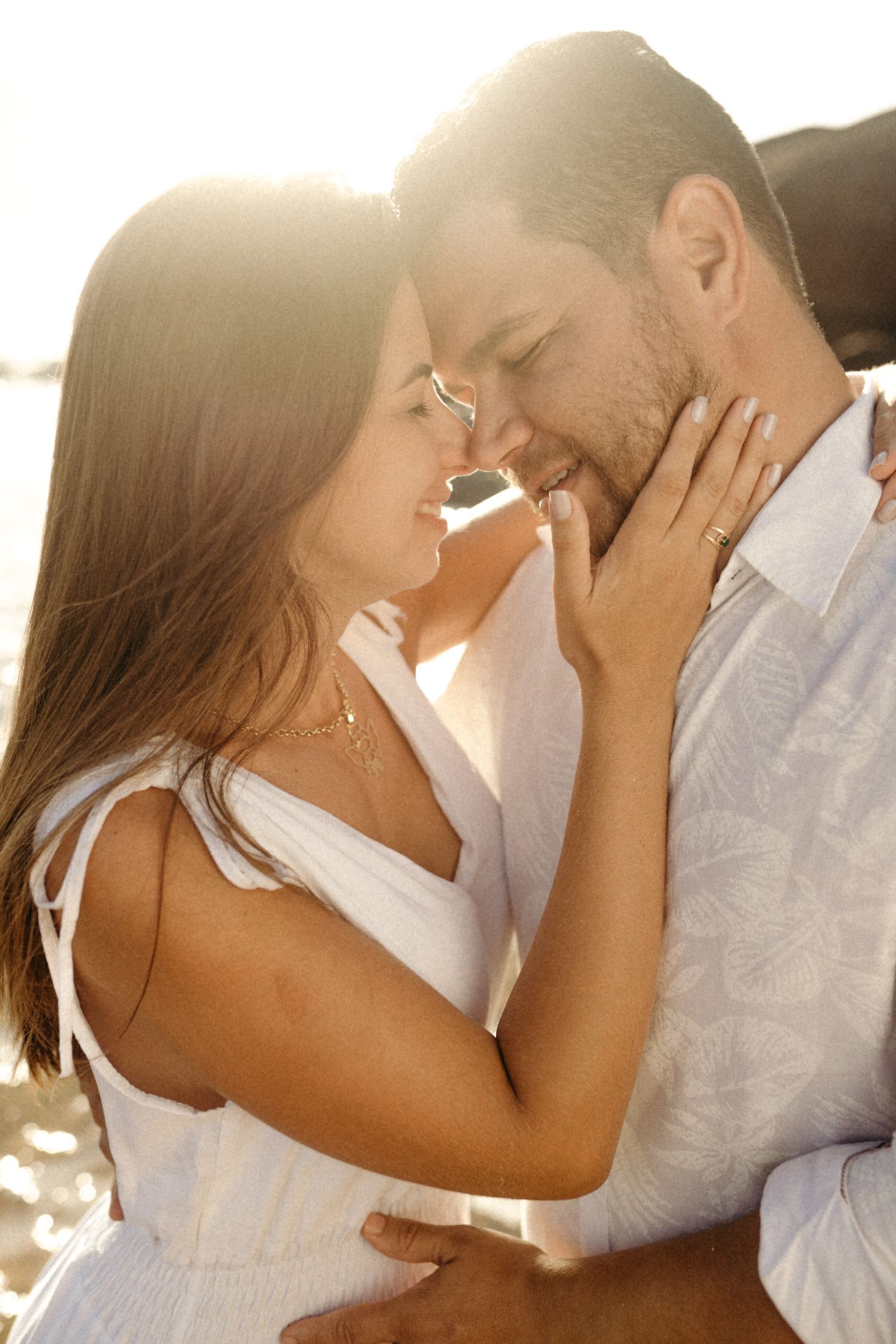 Romantic couple sharing tender moment in white outfits during golden hour photoshoot.