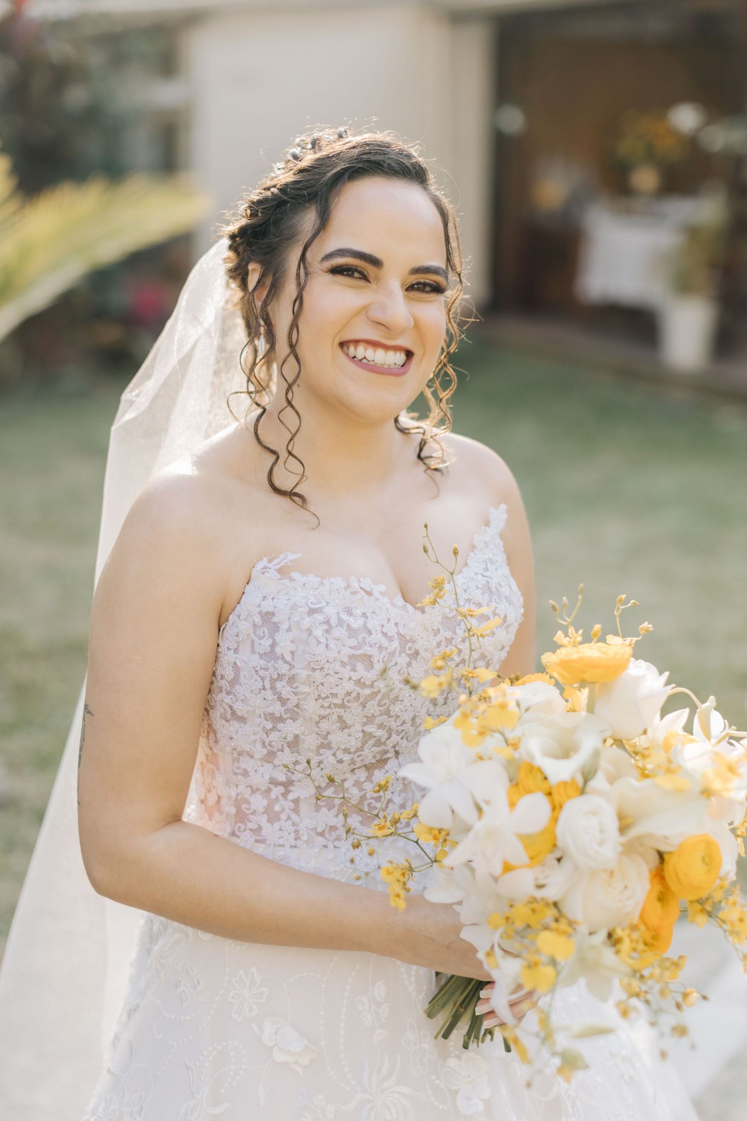 A bride in a strapless lace gown holds a yellow and white bouquet.