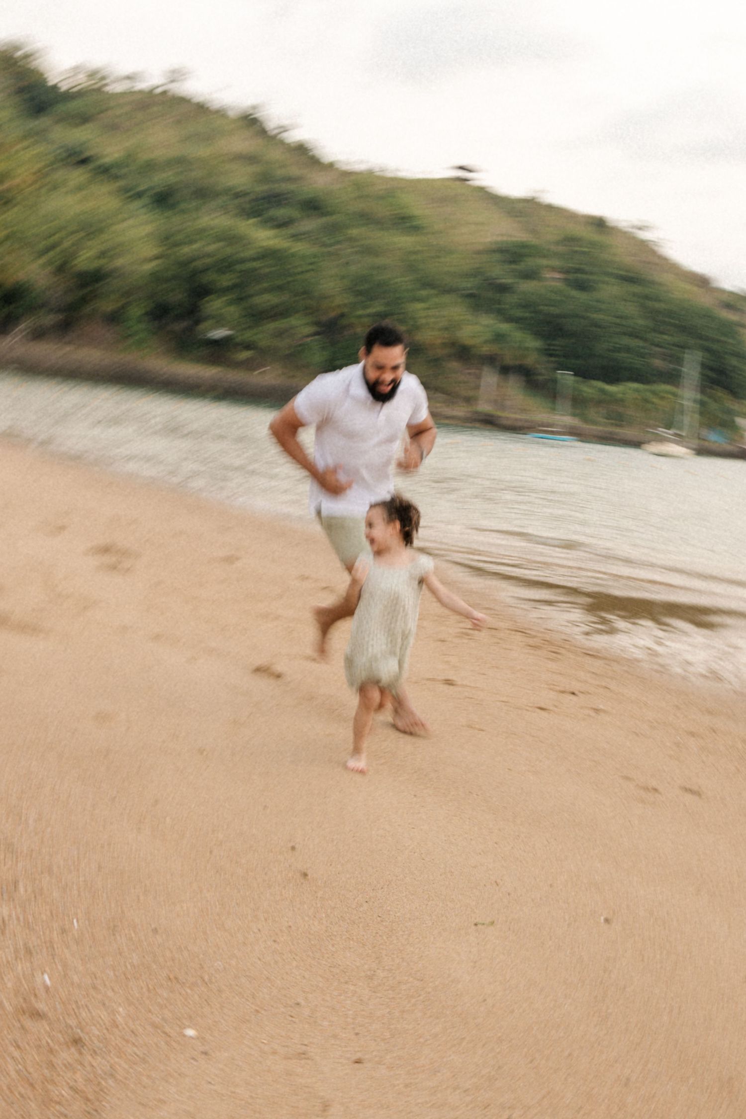 Two people run and play together on a scenic beach with green hills in the background.