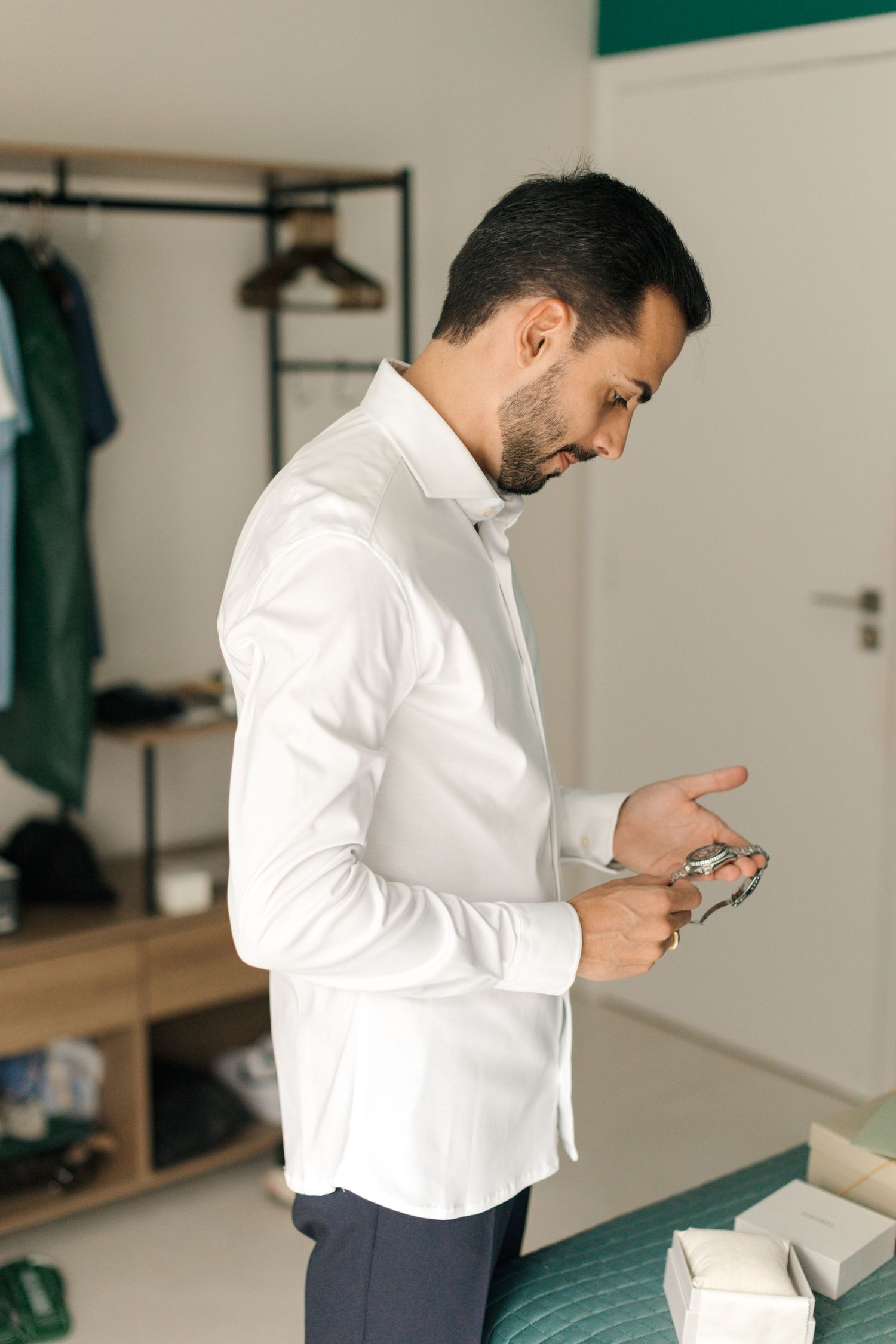 Person in white dress shirt examining a luxury watch in a bedroom setting.