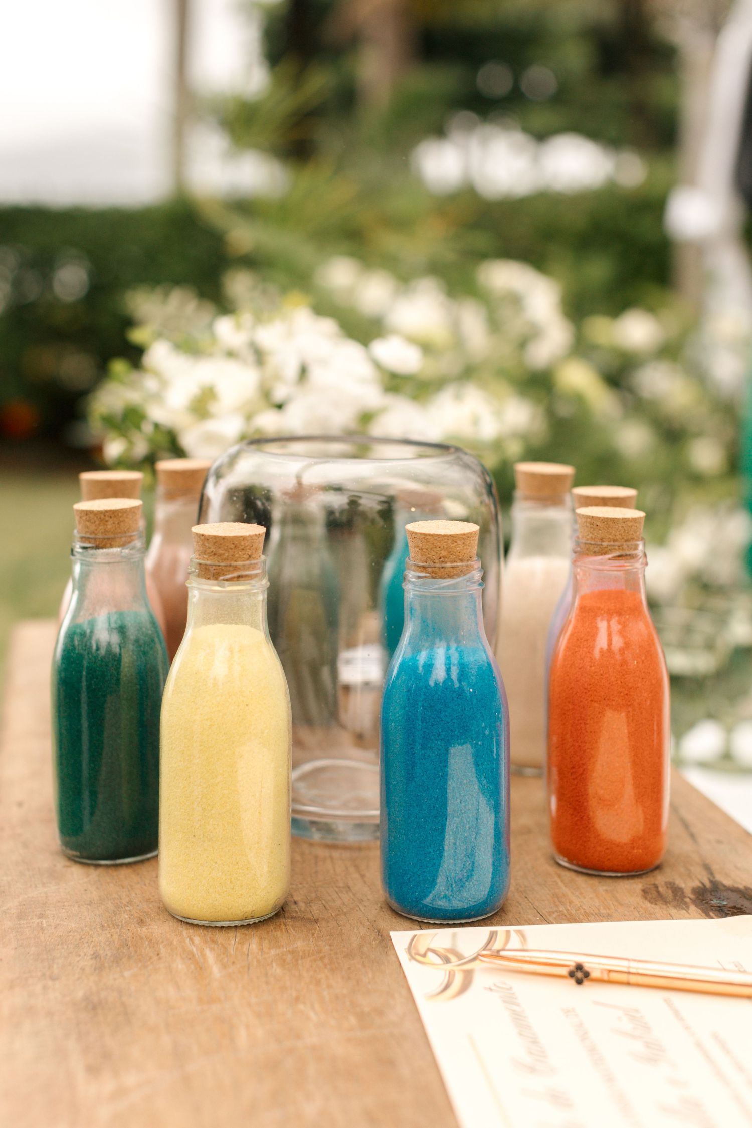 Colorful bottled drinks with cork stoppers arranged on a wooden table at a wedding reception.