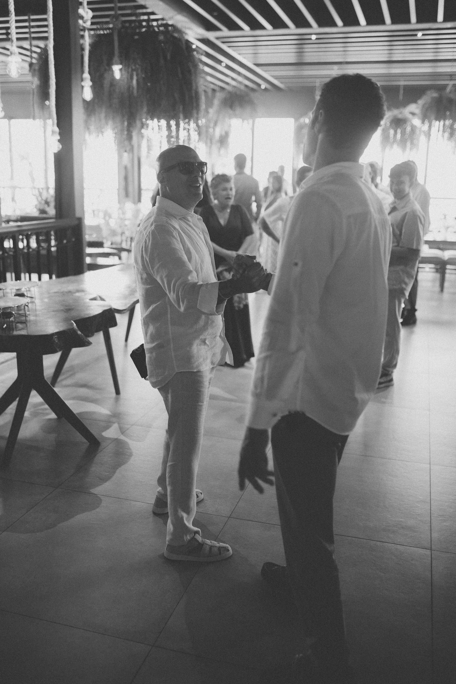 Black and white candid photo of guests mingling at indoor reception venue.