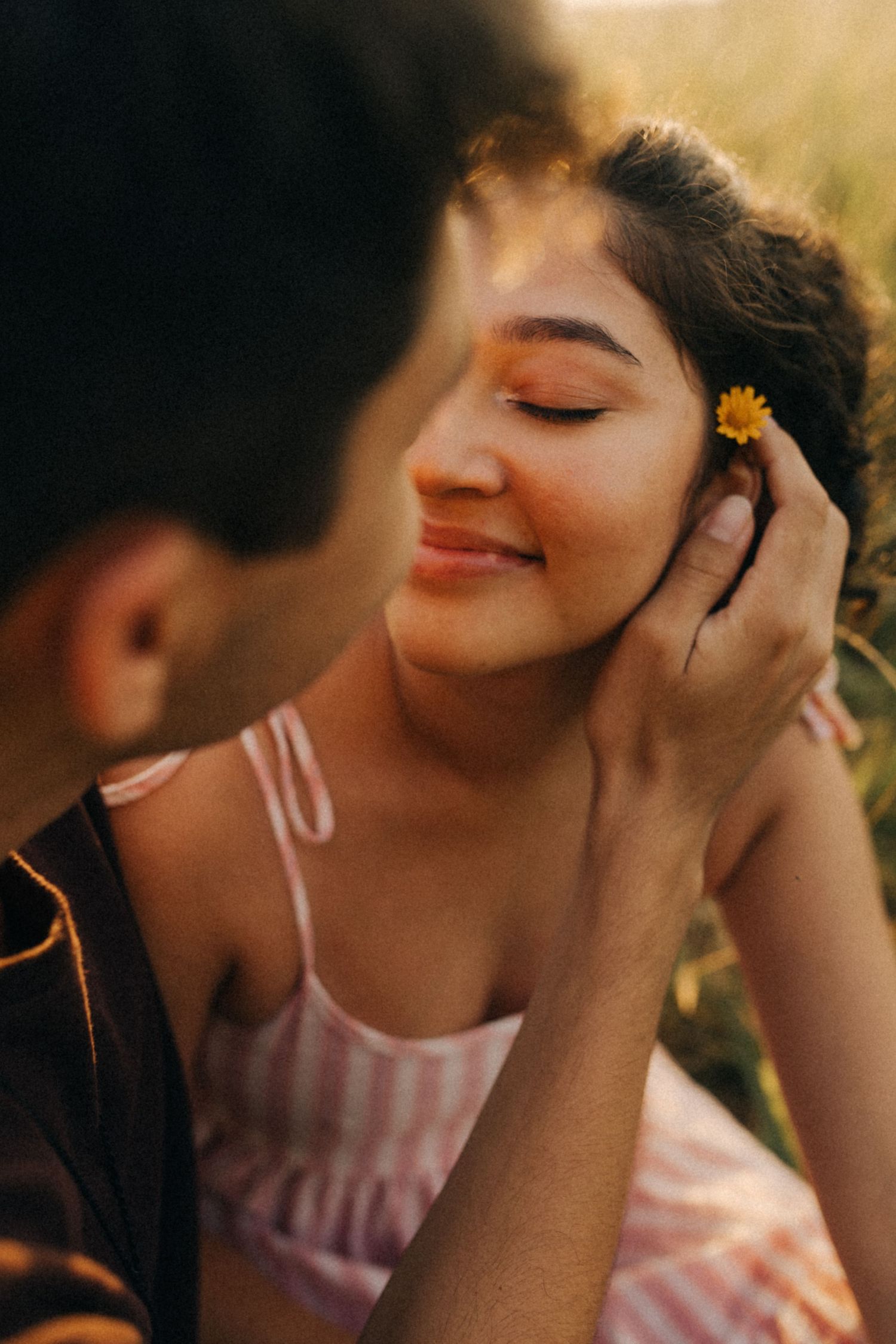 Um momento romântico capturado durante a golden hour, quando uma pequena flor amarela é colocada atrás da orelha em um dia  quente de verão.