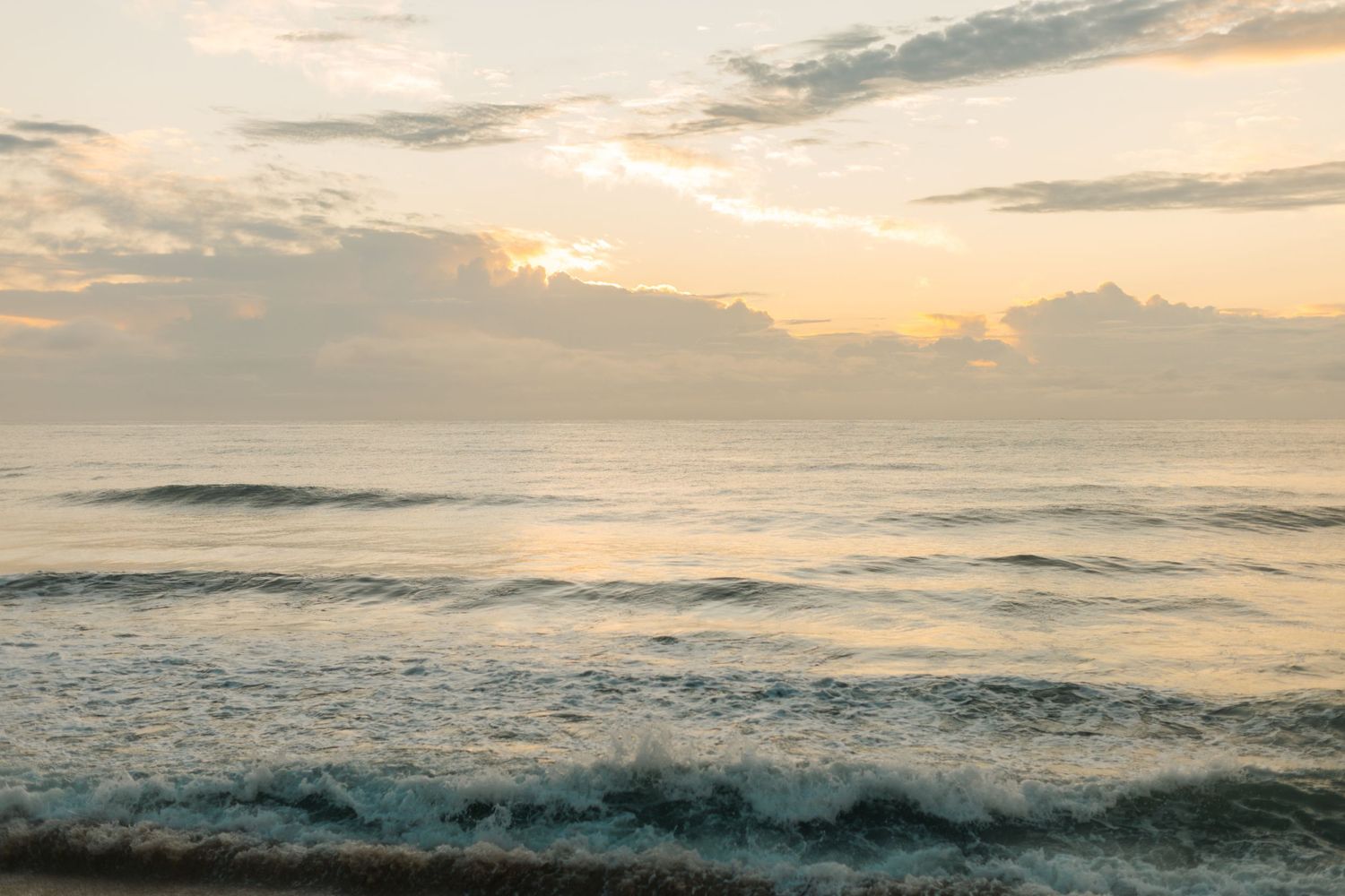 Peaceful ocean waves rolling onto shore during a golden sunset with wispy clouds in the sky.