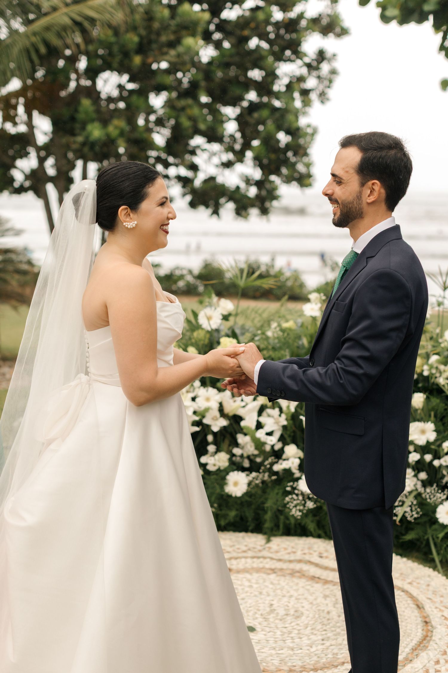 Couple exchanging vows in garden setting surrounded by white flowers and greenery.