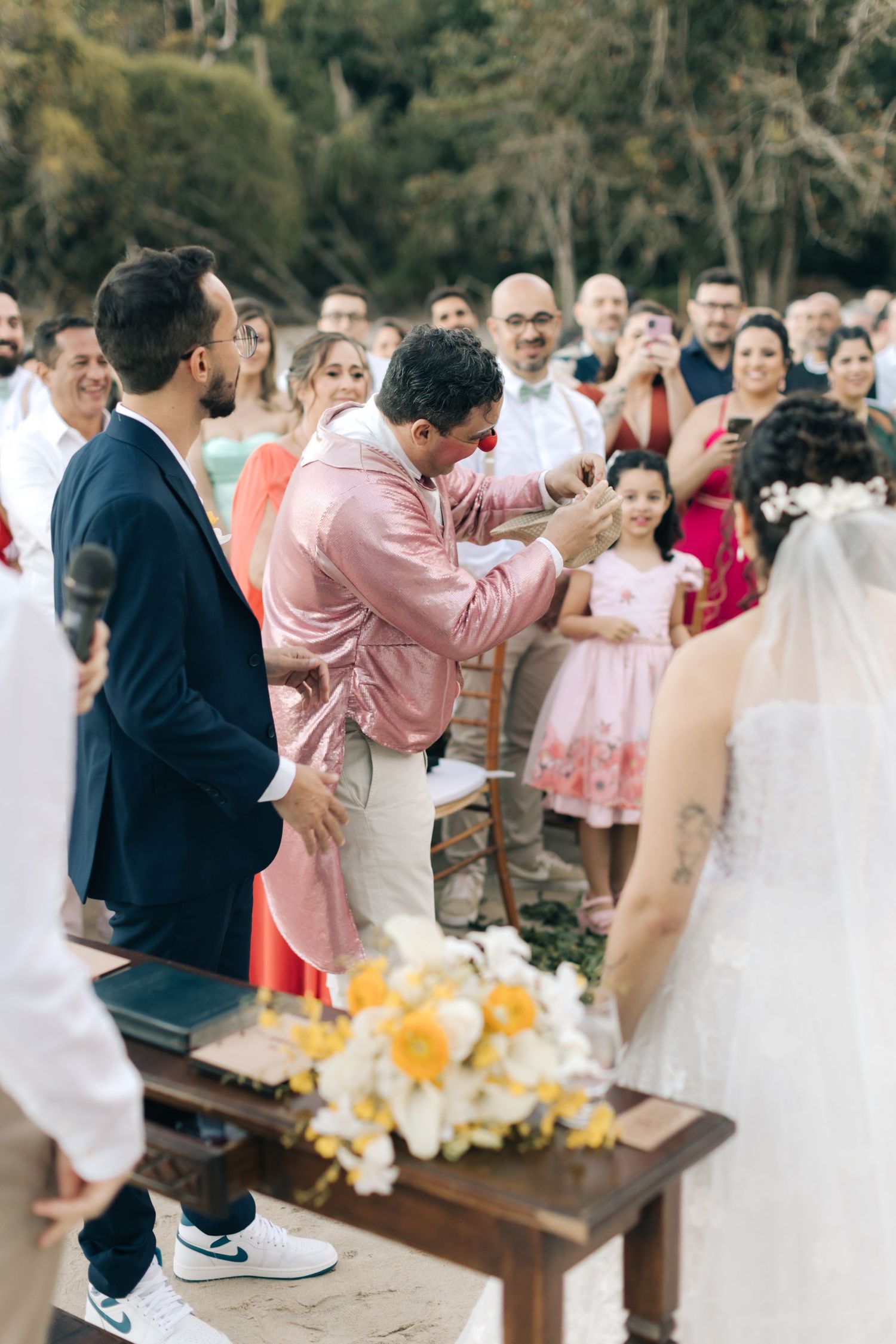 Wedding guest shows enthusiastic reaction during outdoor ceremony next to floral arrangement.