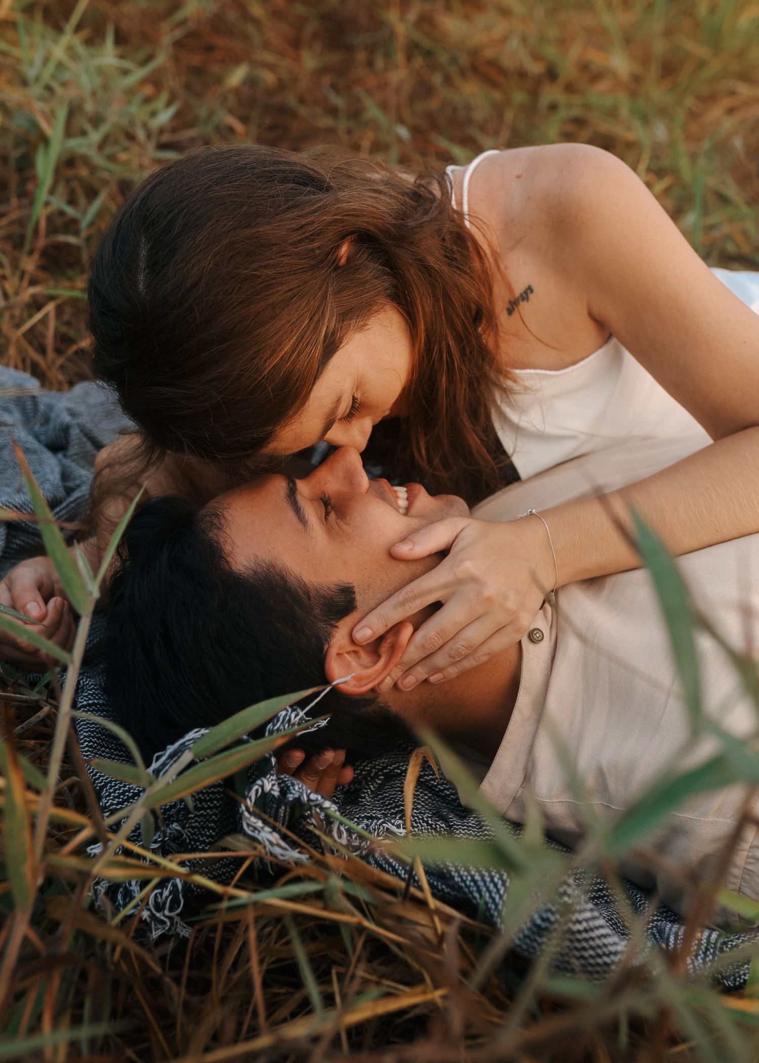 Romantic couple lies intimately in tall grass during sunset photoshoot.