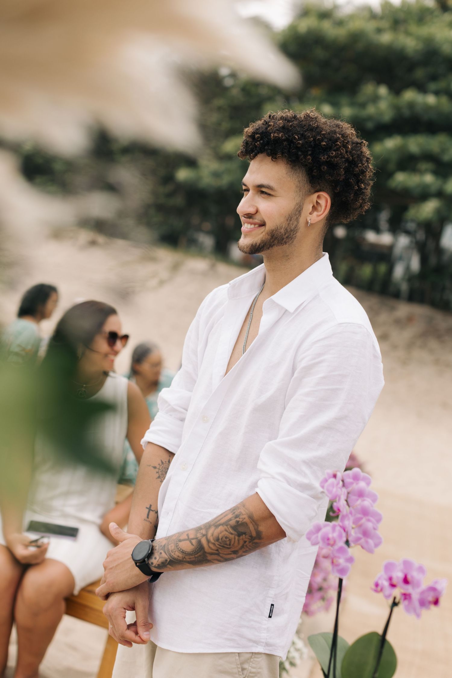 Wedding guest in casual white attire smiling during beachside celebration.