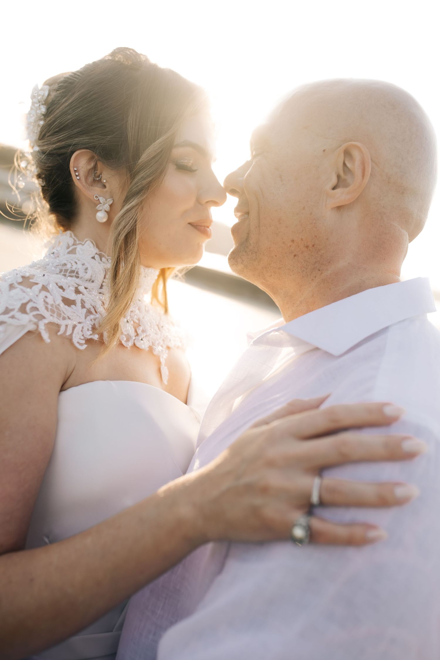 A romantic dip pose between two people in wedding attire with sunlight streaming behind them.