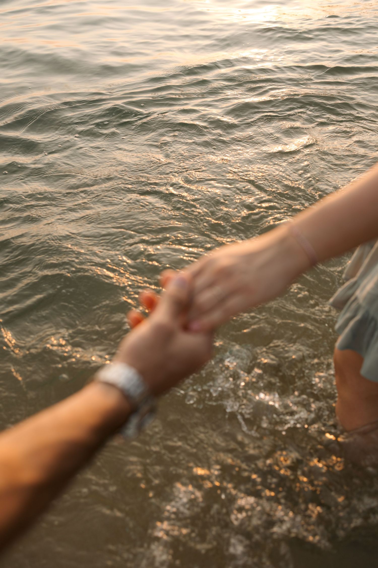 Hands reaching out to hold each other over glistening ocean water.