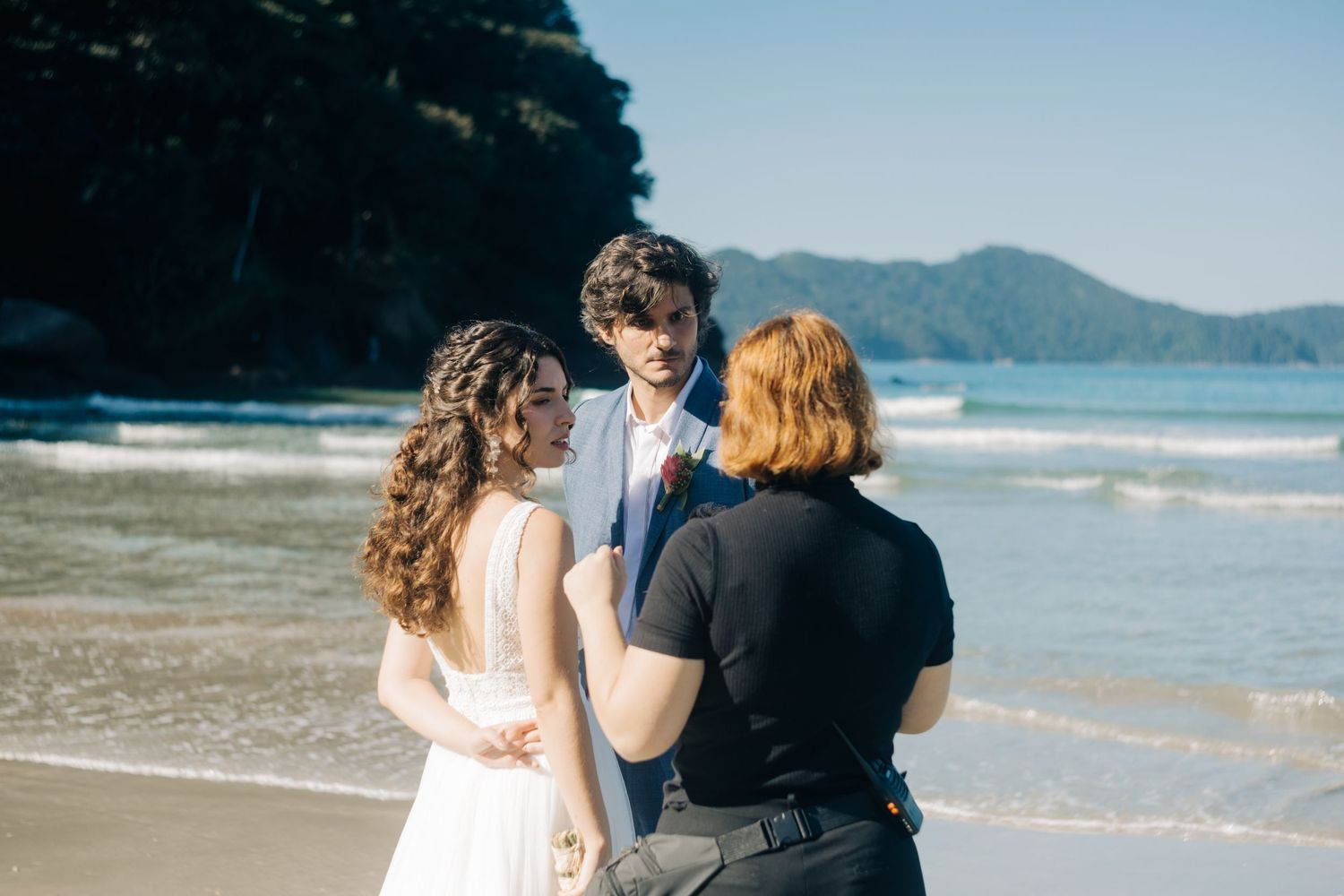 Couple standing together on a scenic beach with mountains in the background.