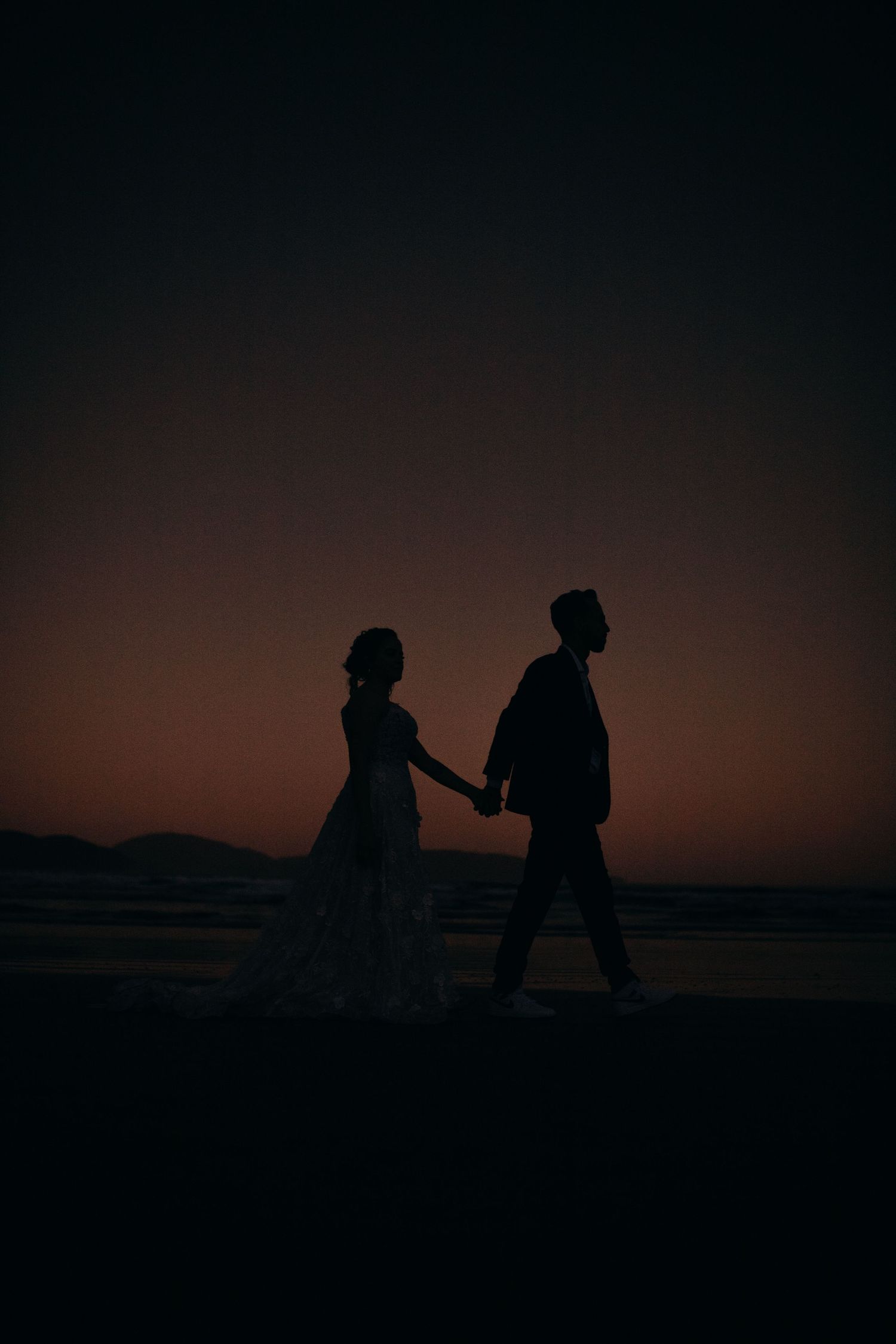 Silhouetted couple walking on beach at sunset.