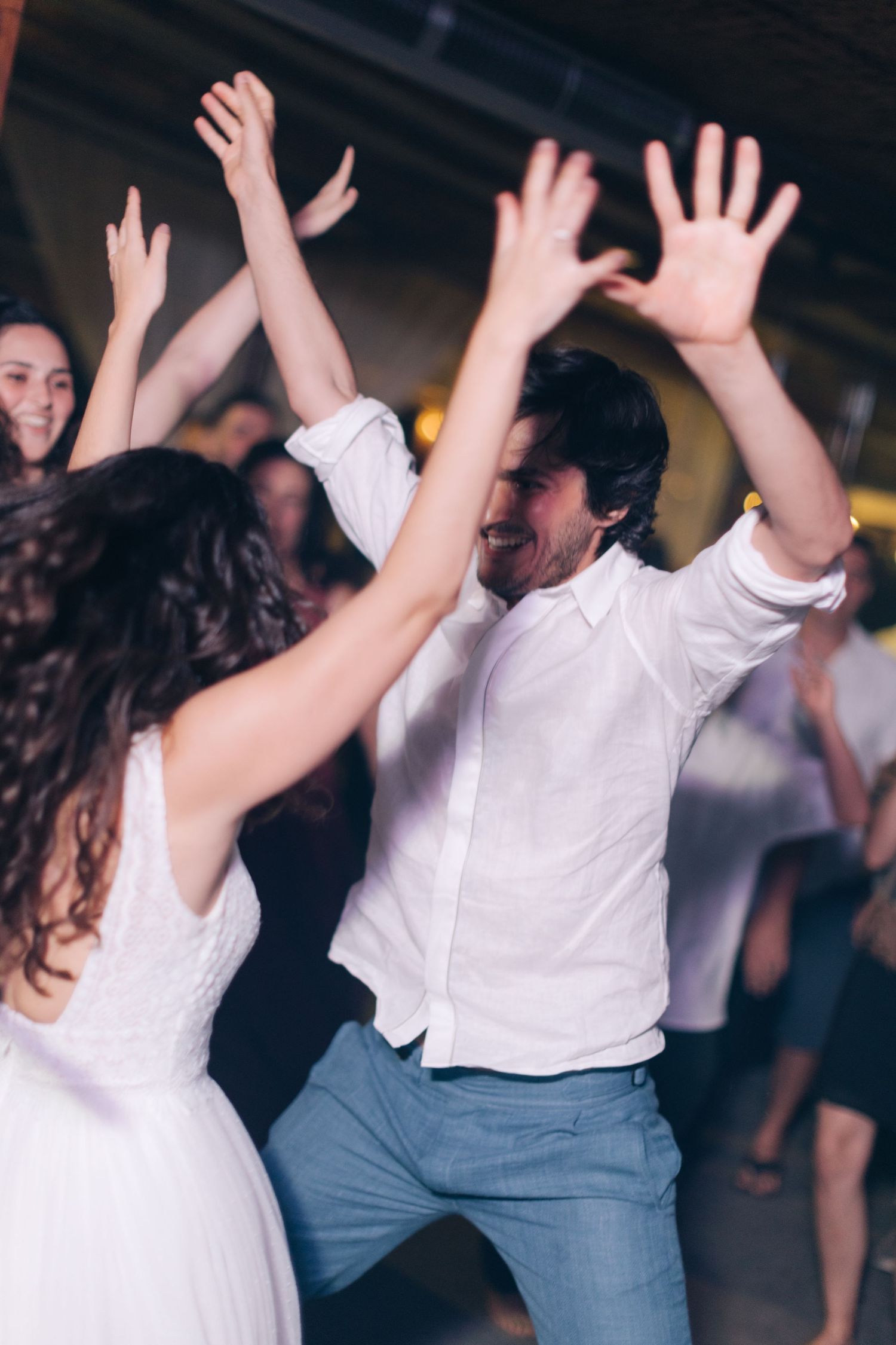 Two people dance energetically with raised arms at a wedding celebration.