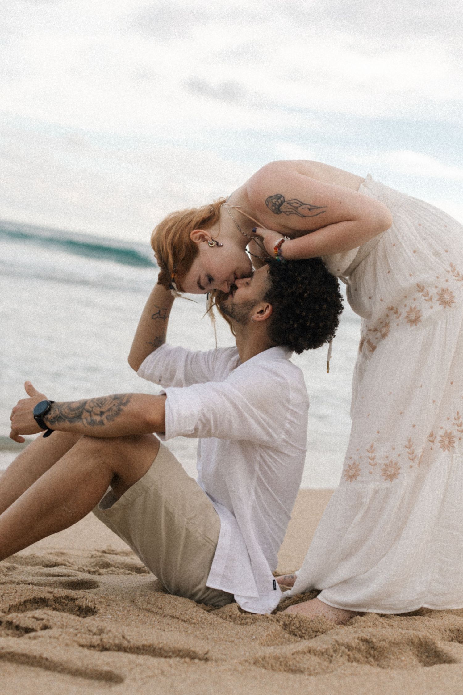 A playful couple shares a romantic moment while sitting on the beach sand.
