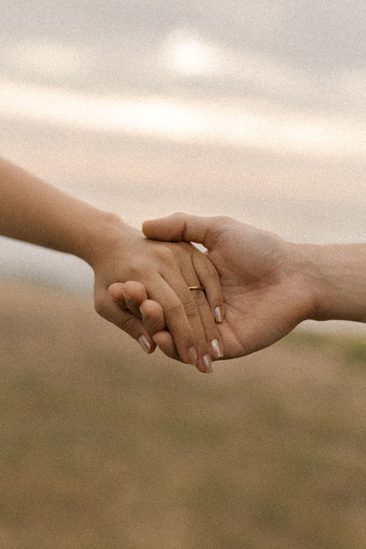Close-up shot of two hands clasped together with wedding rings showing against a soft, blurred background.