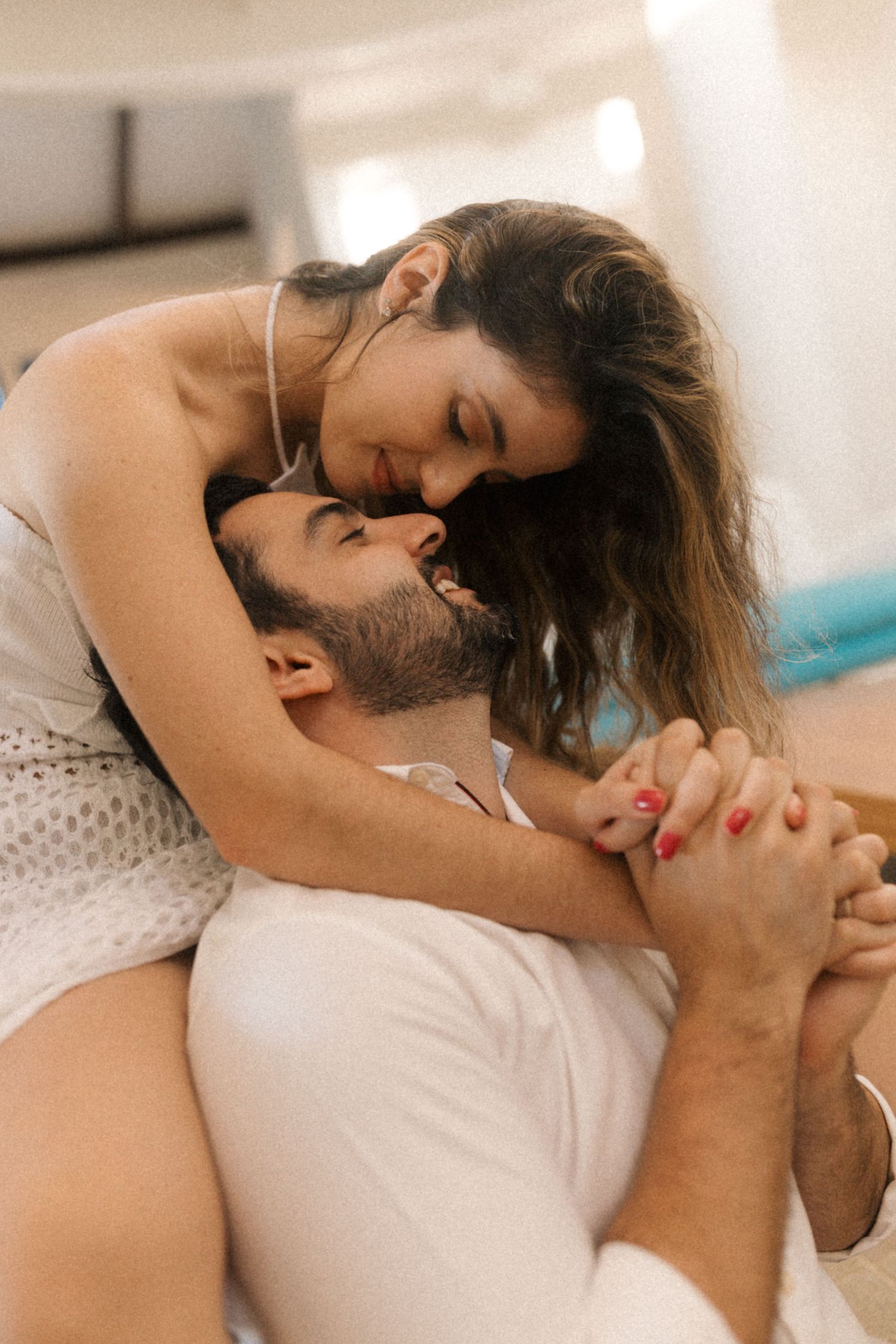 Intimate couple sharing tender moment on white furniture in sunlit room.