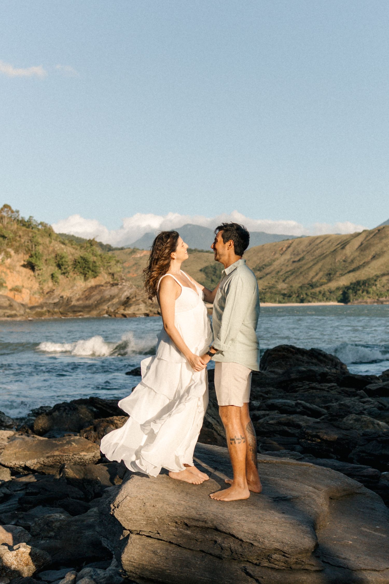 A romantic coastal photo session with mountains and crashing waves in the background.