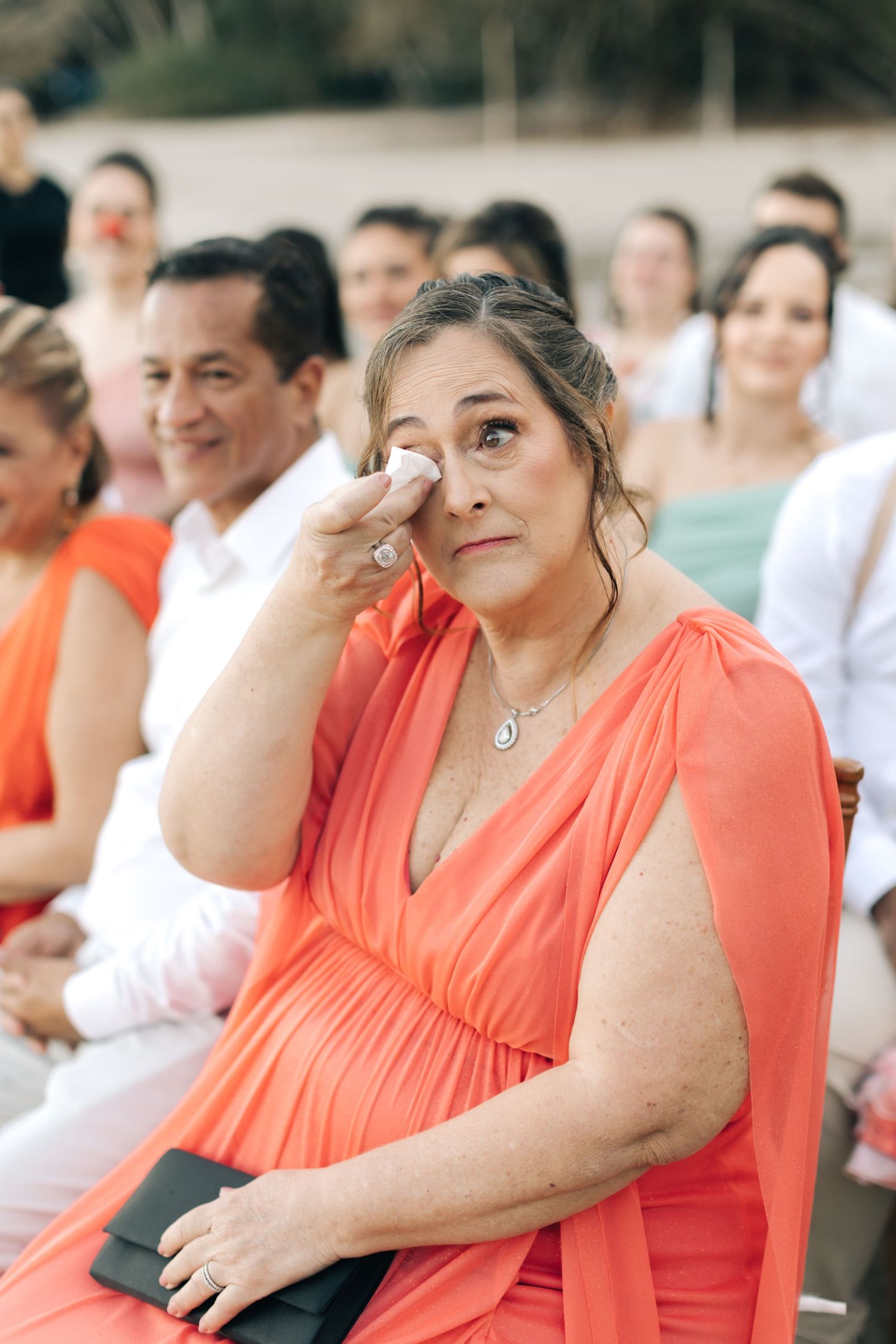 Wedding guests in coral dresses sitting outdoors during a beach ceremony.