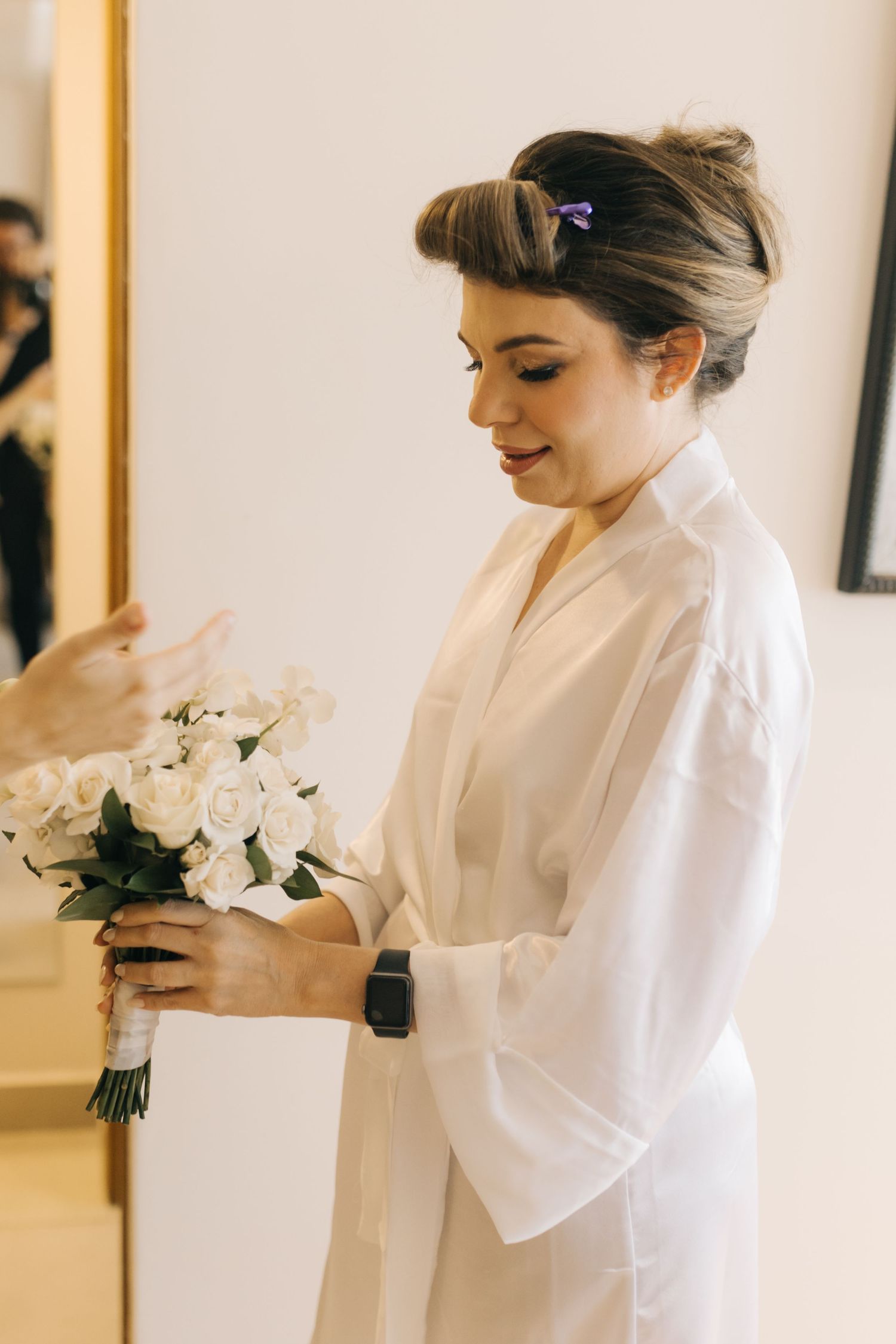 Bride in white robe admiring her wedding bouquet while getting ready.