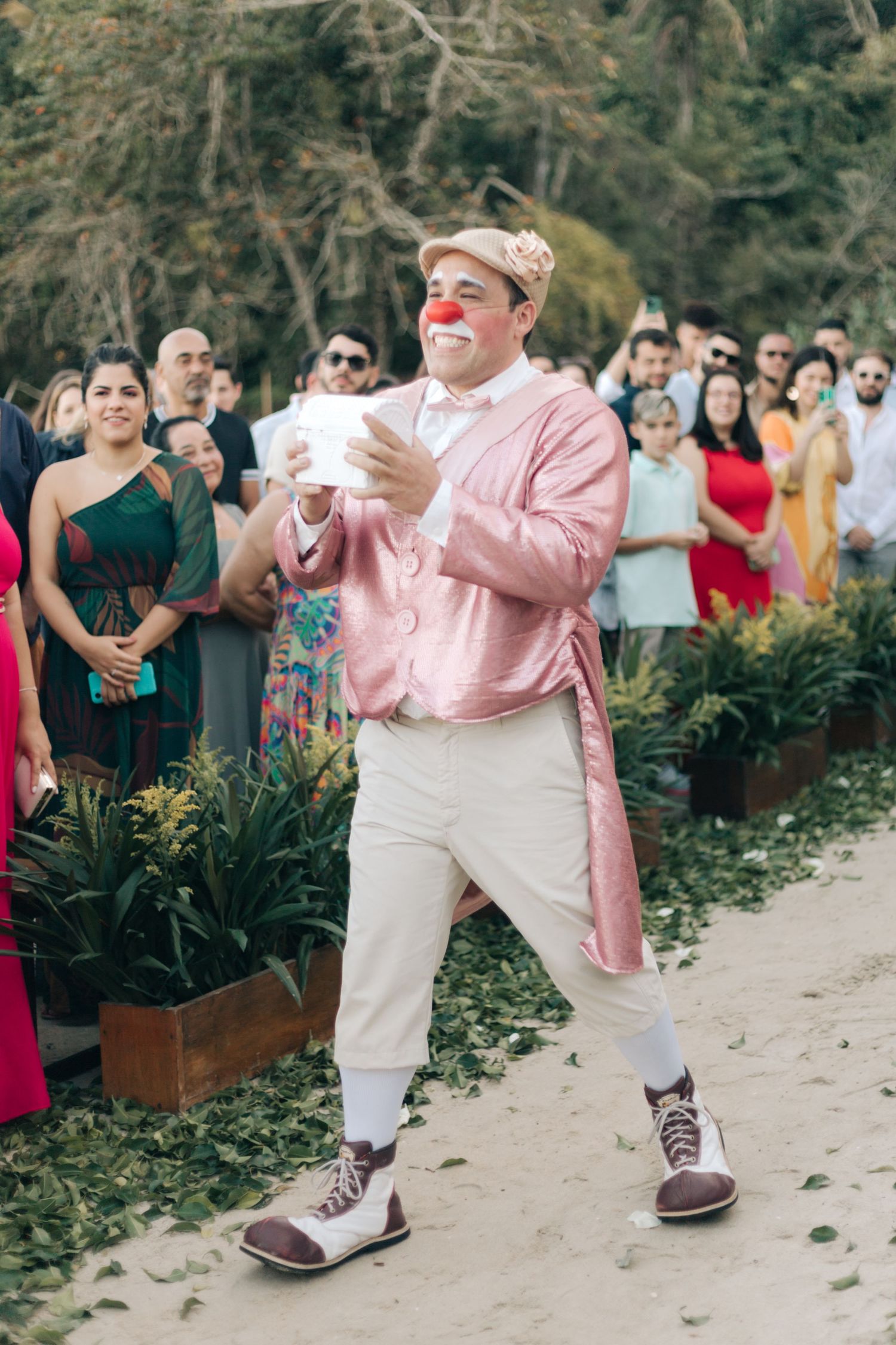 Entertainer in pink attire and red nose performs with paper cups at outdoor event.
