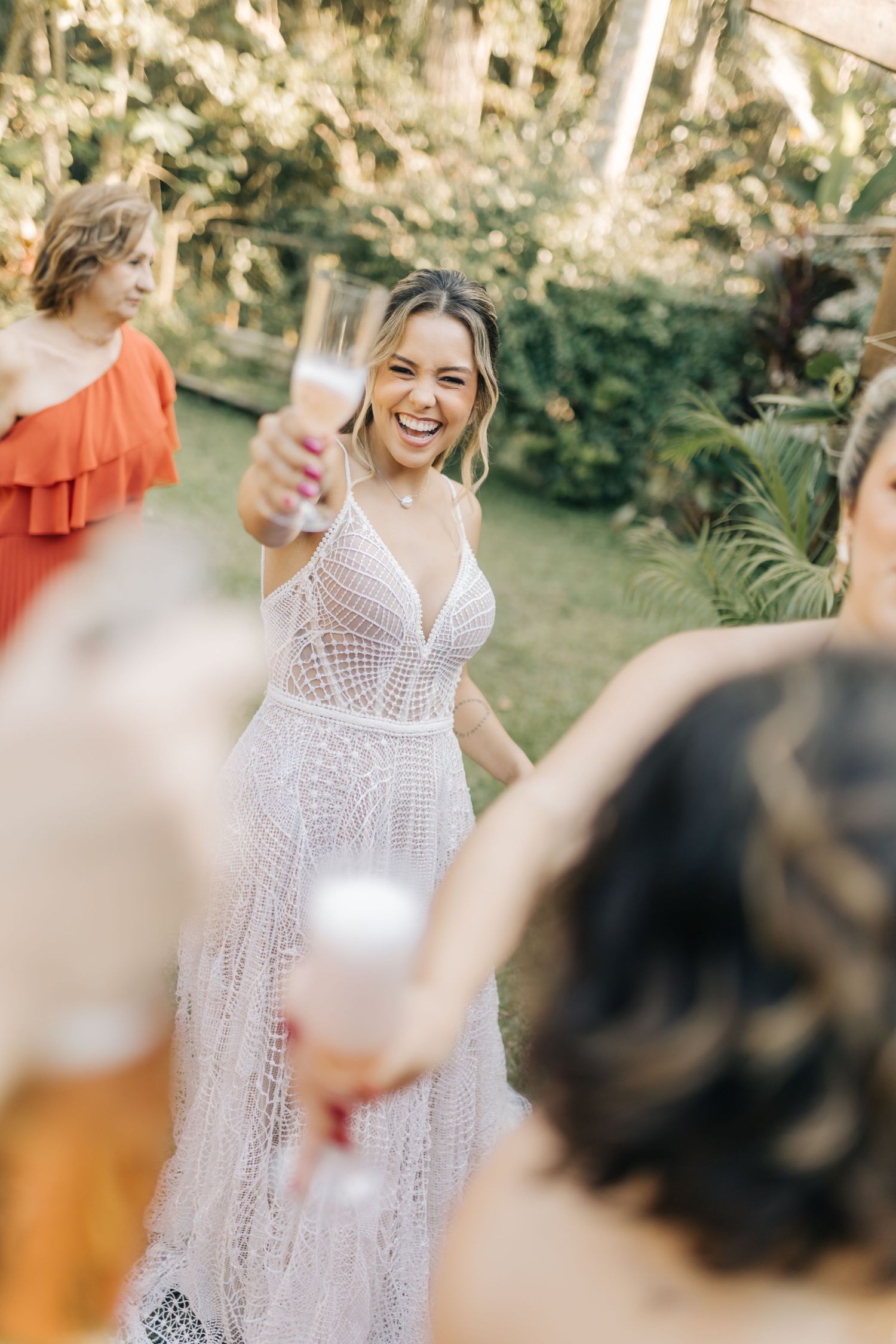 A person in an intricate white wedding dress raises a glass during an outdoor celebration.
