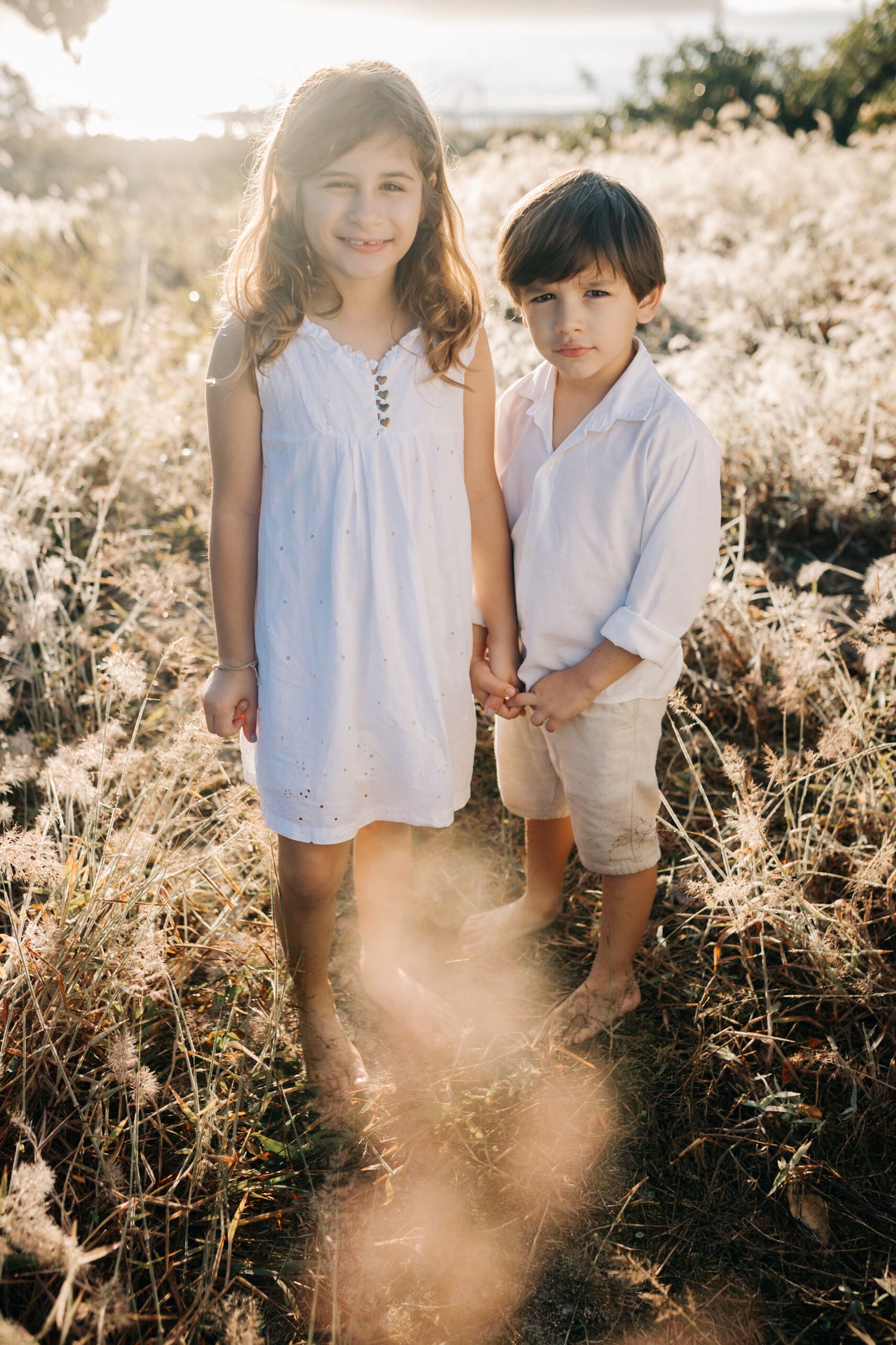 Two young siblings pose together in a golden field during sunset.