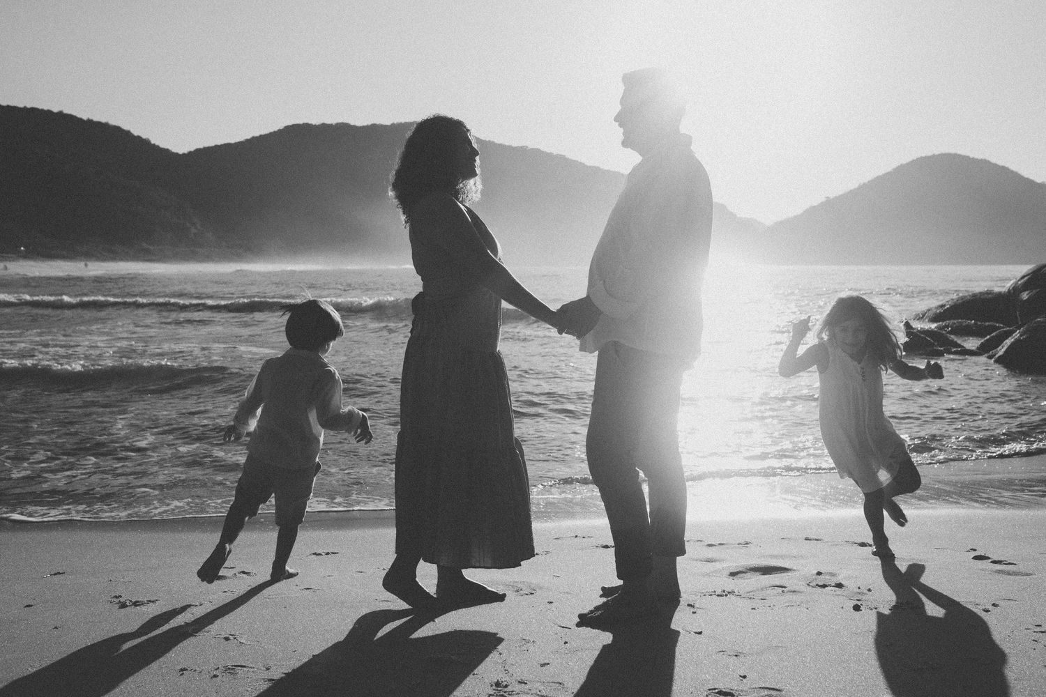Silhouette of family standing on beach at sunset with mountains in background.
