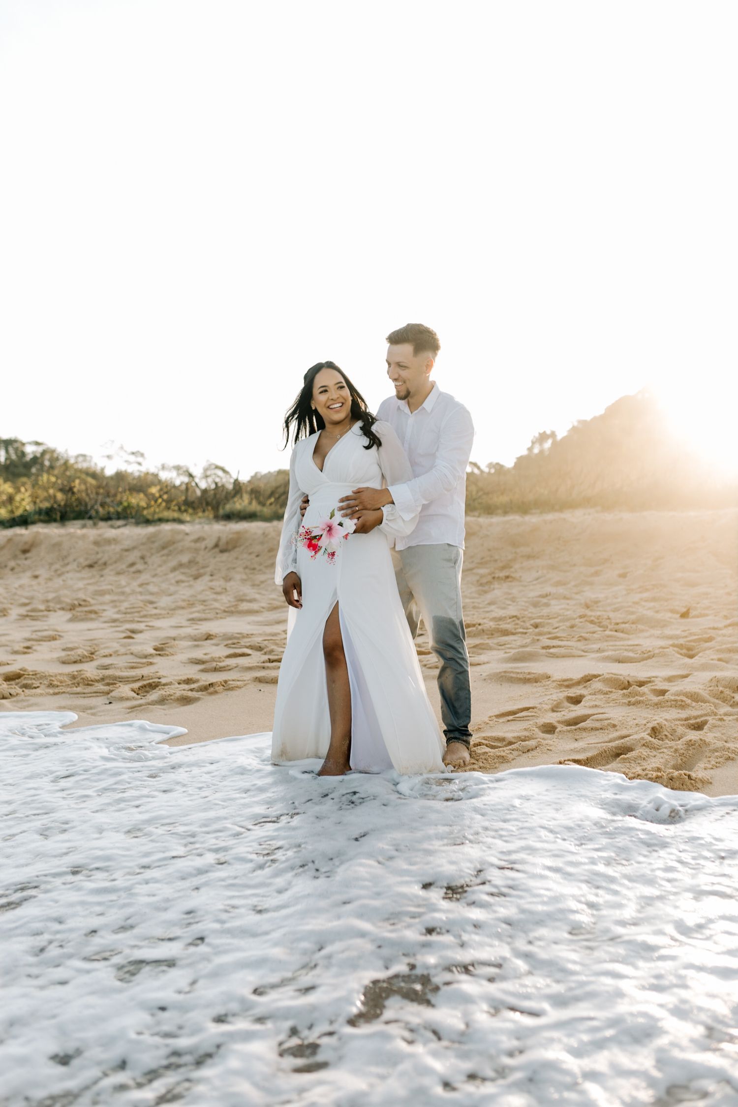 Sun-drenched beach photoshoot features couple in white outfits playing in sand.