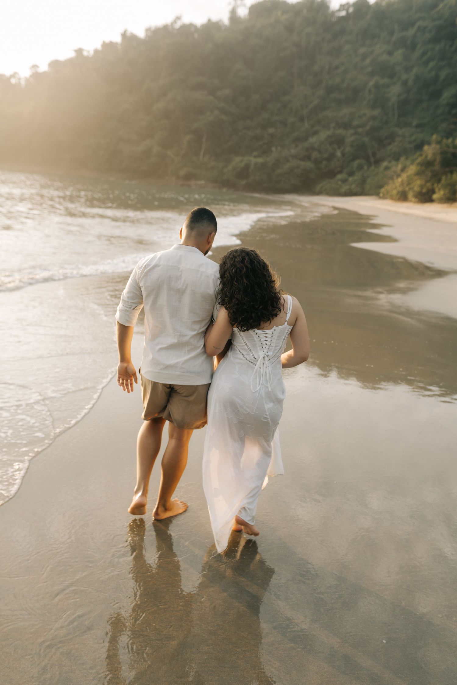 A couple walks hand in hand along a sunset beach shoreline.