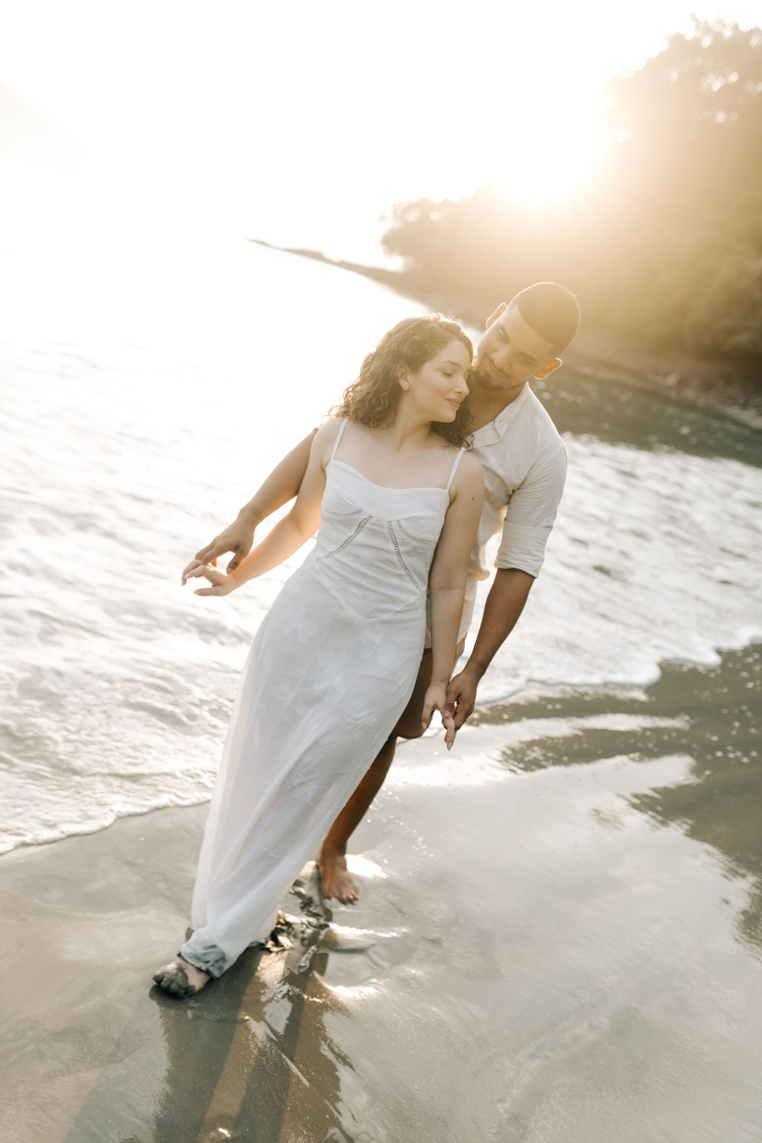 Couple dancing playfully on the beach during a golden hour photography session.