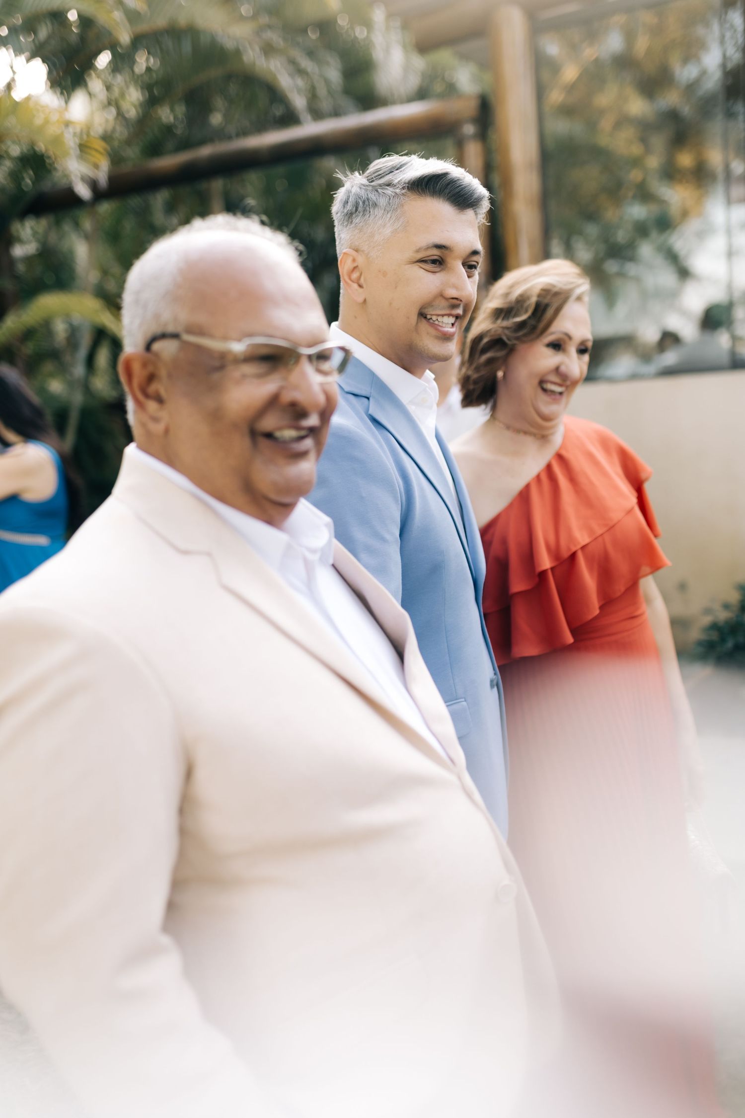 Wedding guests in formal attire smile during an outdoor celebration.