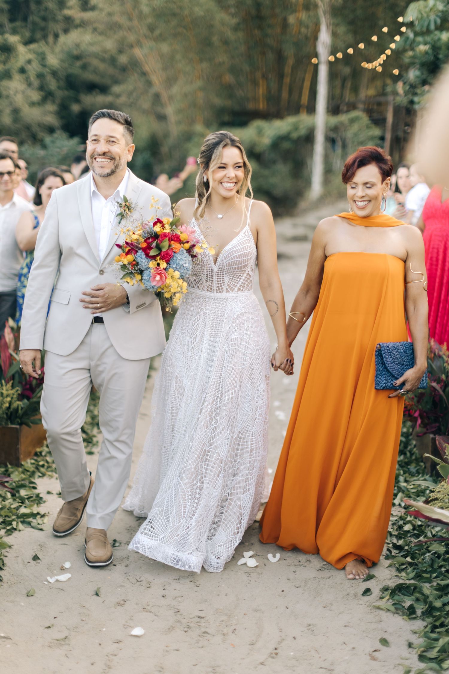 Wedding party walking down garden path with vibrant orange dress and colorful bouquet details.