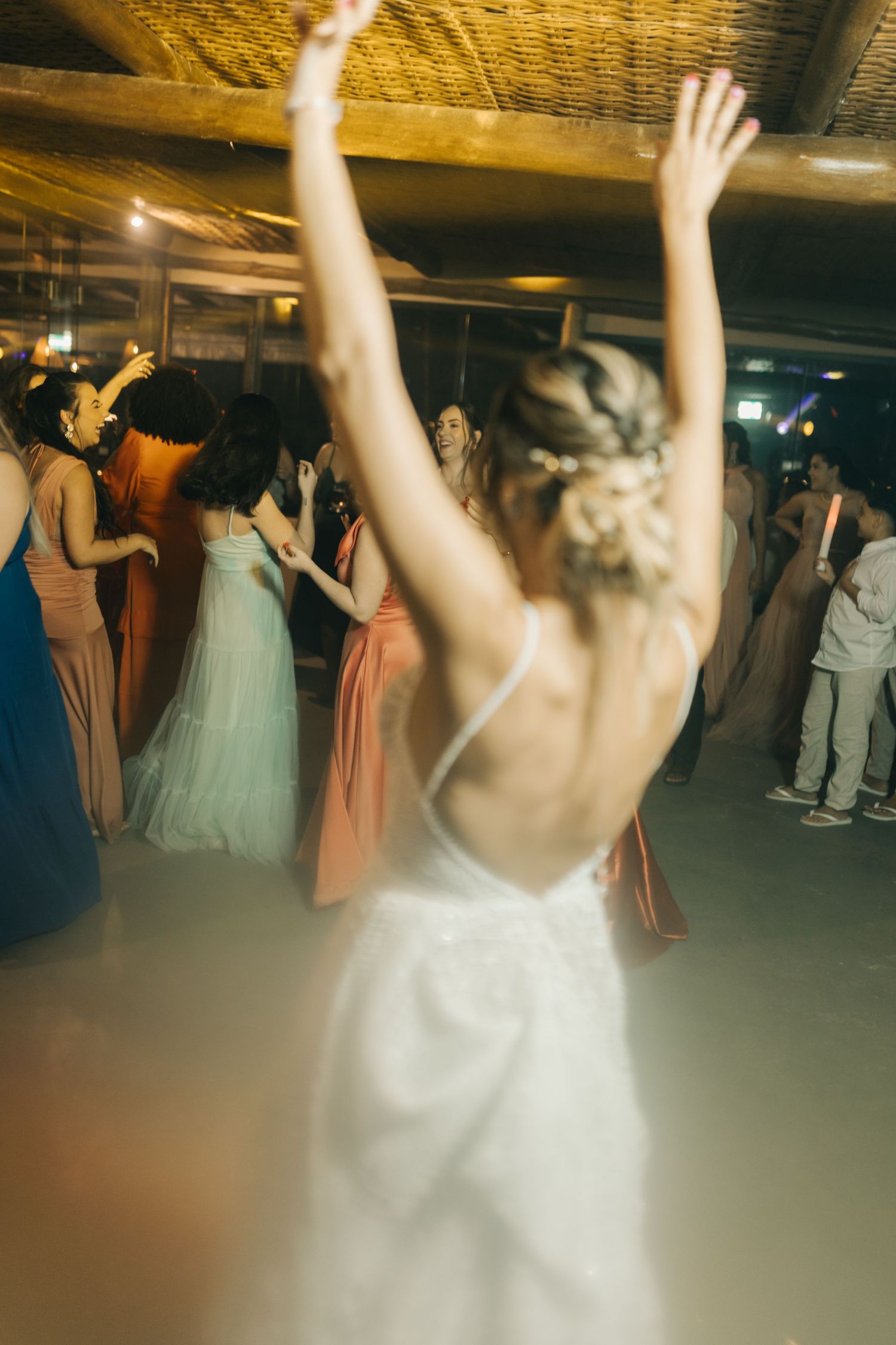 Low angle view of wedding guests dancing with hands raised under decorative lighting.